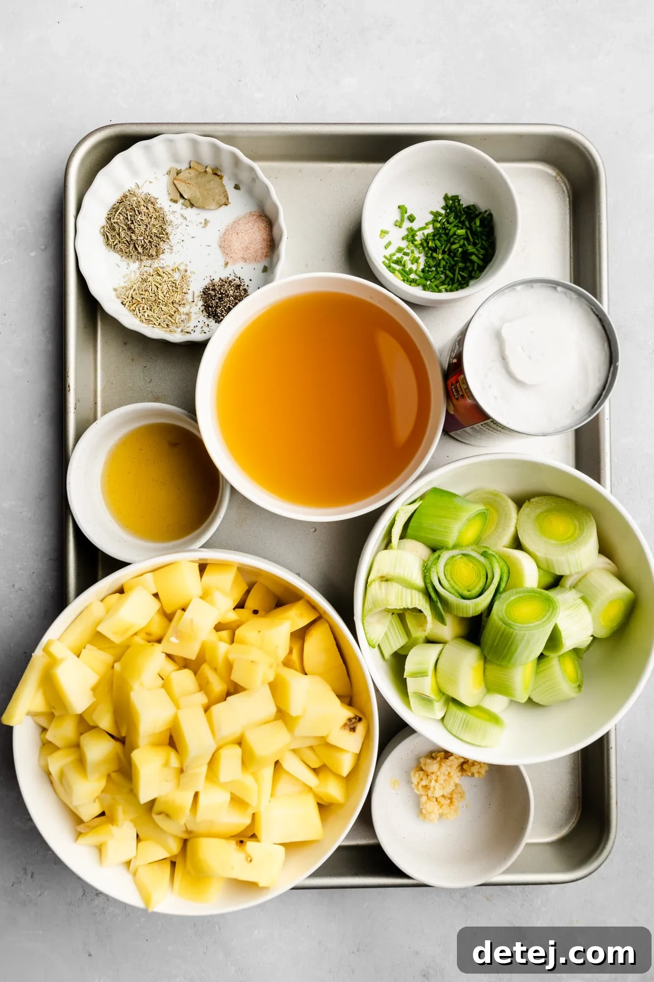 Individual white bowls arranged on a metal tray, showcasing all the fresh and prepared ingredients ready for making Vegan Potato Leek Soup, emphasizing freshness and organization.