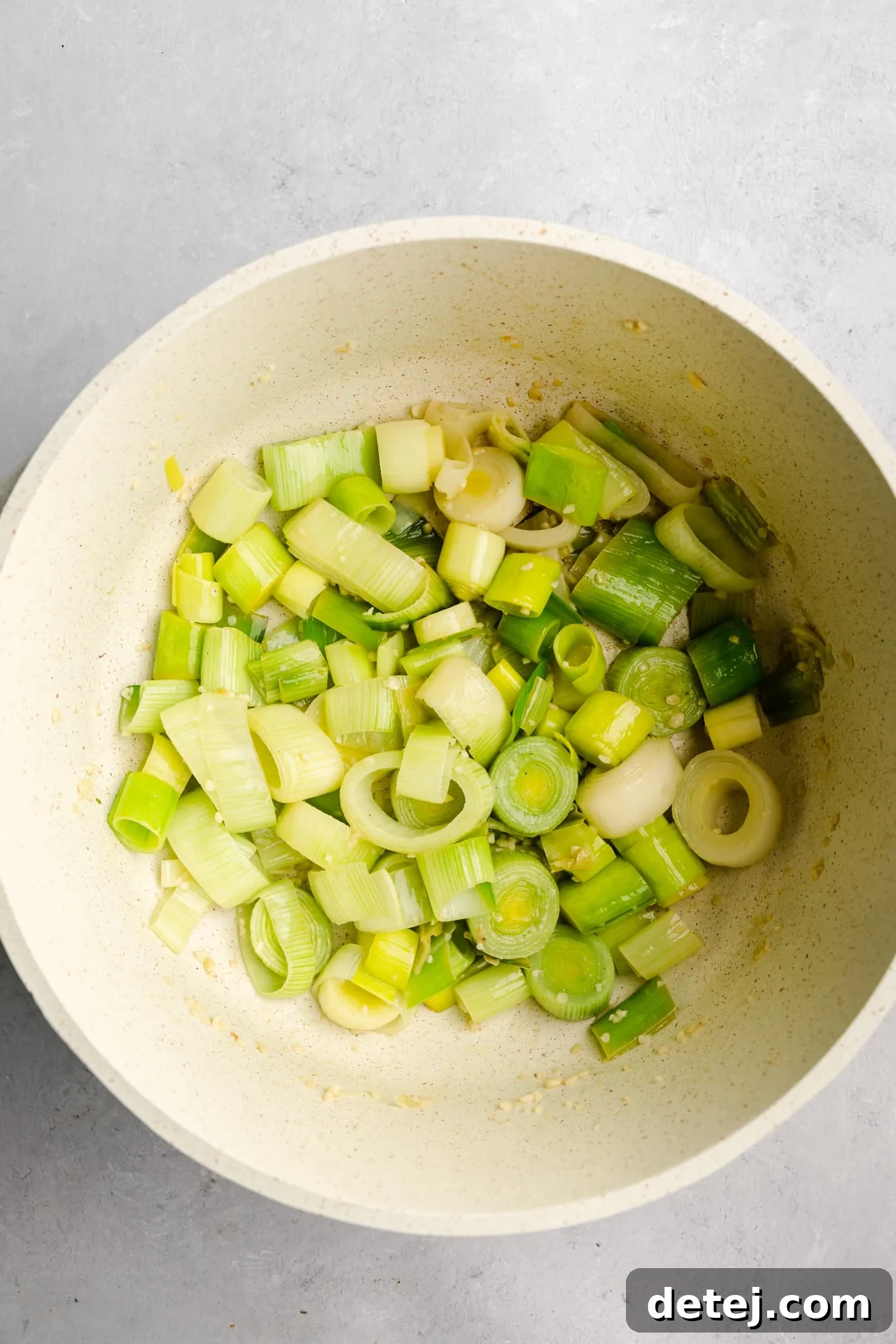A large white pot on a stove with perfectly sautéed leeks and garlic, emitting a fragrant aroma, ready for the next steps of making the soup.