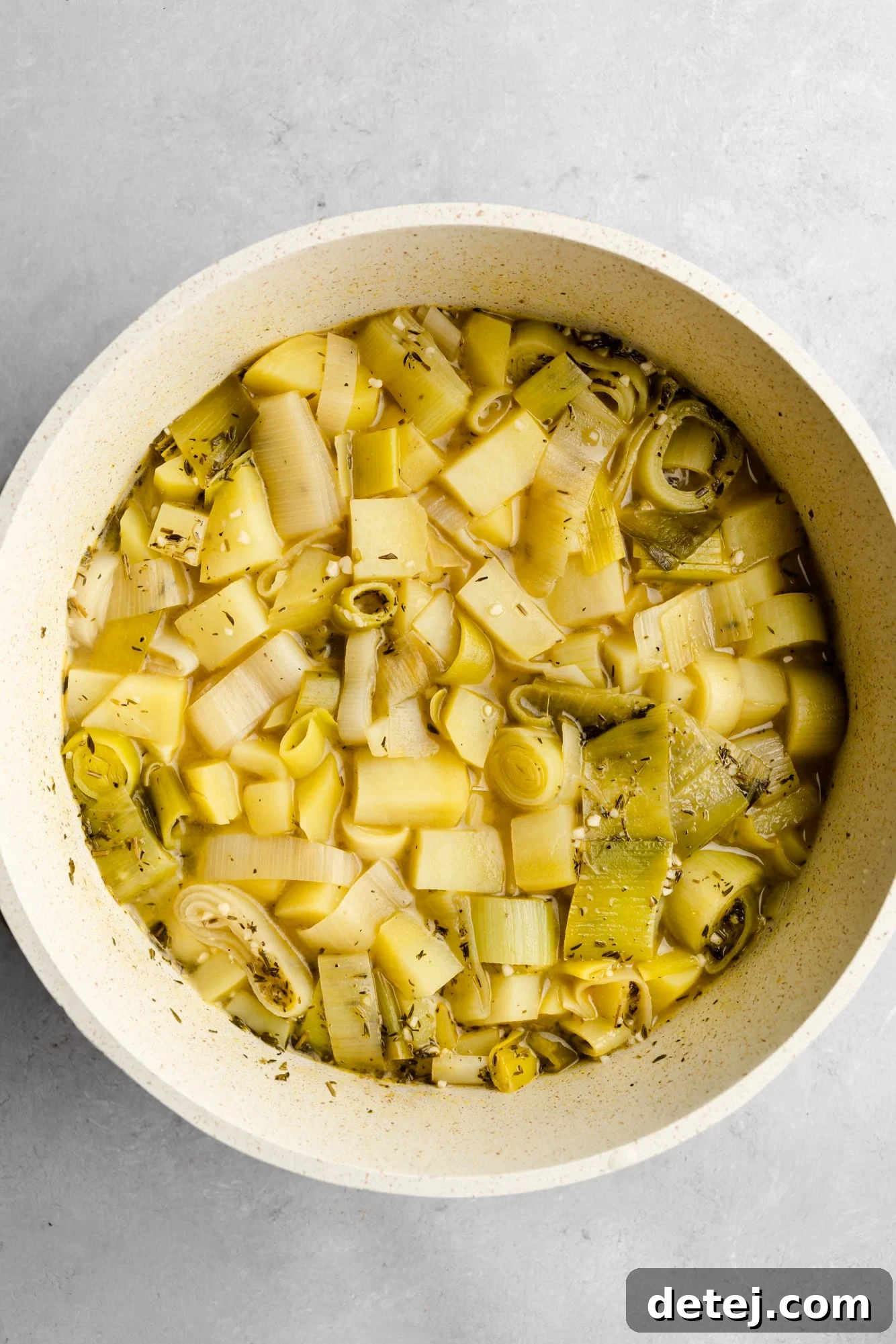 The Vegan Potato Leek Soup simmering gently in a large white pot on the stovetop, with all ingredients combined and cooking to perfection.