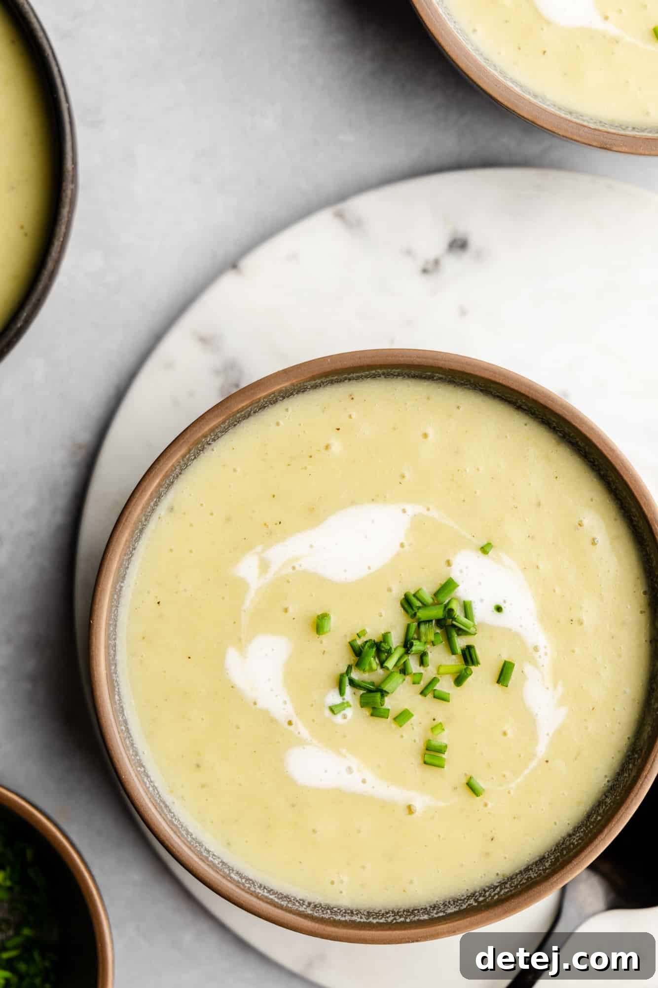 Overhead view of a single bowl of creamy Vegan Potato Leek Soup, elegantly topped with a swirl of coconut cream and a sprinkle of fresh chives, ready to be enjoyed.