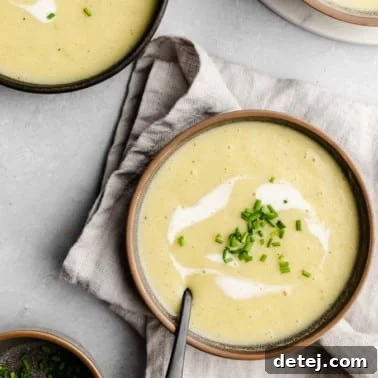 Overhead view of a bowl of Vegan Potato Leek Soup topped with coconut cream and chives, presented beautifully in a round image format.