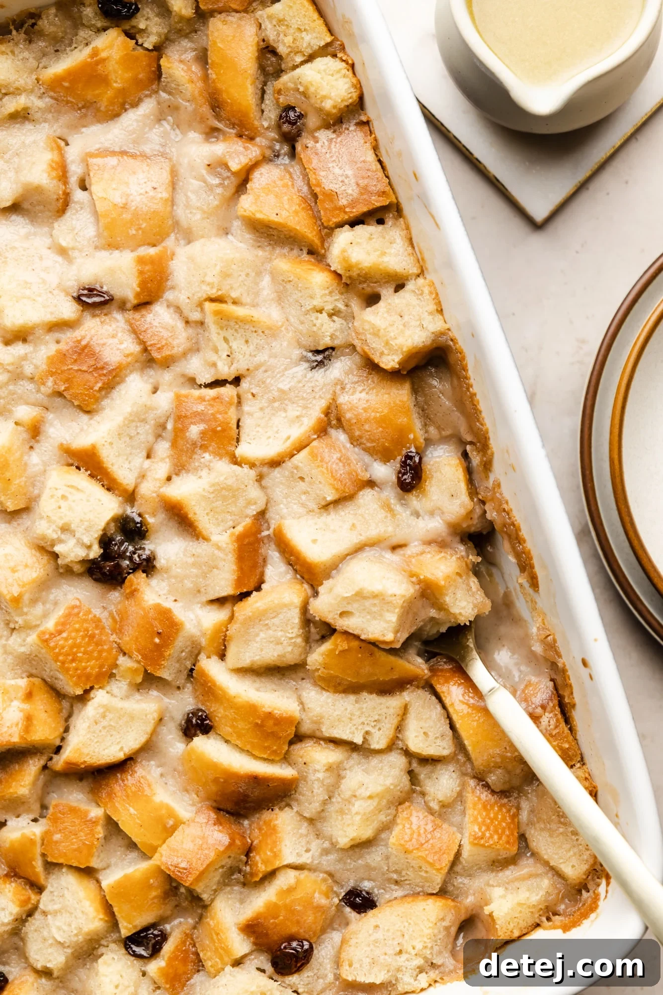 Decadent Vegan Bread Pudding 2 A golden-brown slice of vegan bread pudding, glistening with bourbon glaze, being scooped from a white baking dish with a spoon.