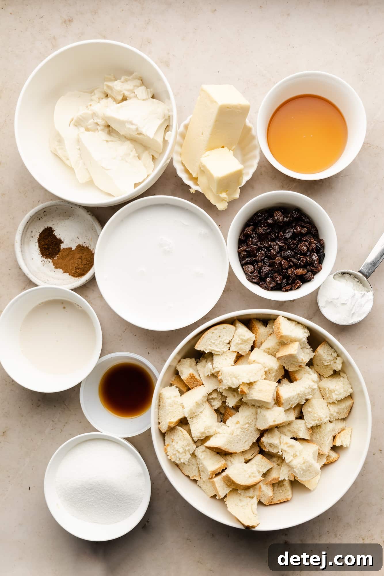 Decadent Vegan Bread Pudding 4 Various ingredients for vegan bread pudding, including bread cubes, raisins, coconut milk, and spices, neatly arranged in individual white bowls.