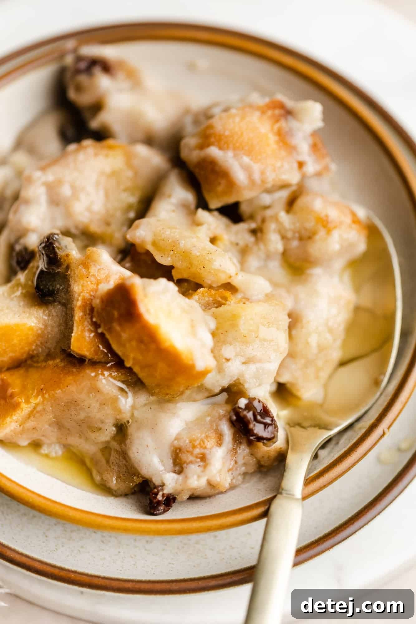 Decadent Vegan Bread Pudding 9 A close-up shot of a scoop of warm vegan bread pudding in a white bowl, with a spoon resting in it, showcasing its soft, custardy texture and glistening glaze.