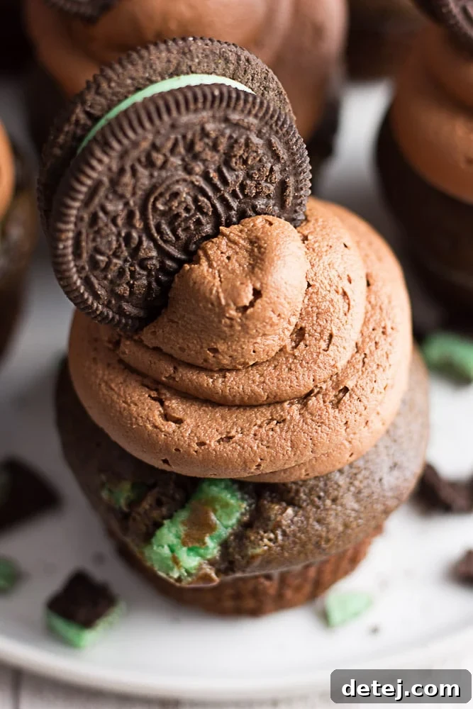 A delicious vegan mint chocolate cupcake, viewed from above, showcasing a generous swirl of green frosting topped with a whole Oreo cookie.