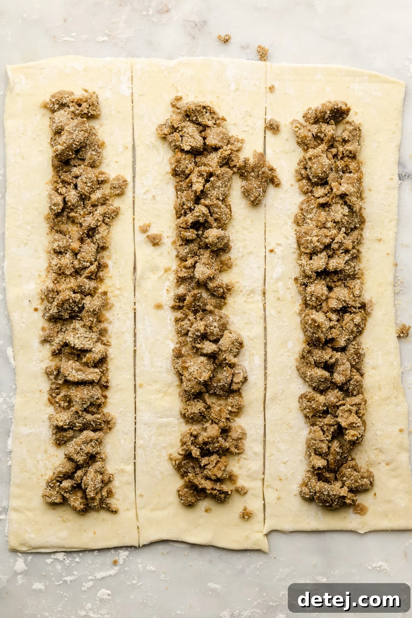 Rows of vegan sausage crumbles precisely placed on sheets of puff pastry, ready for folding.