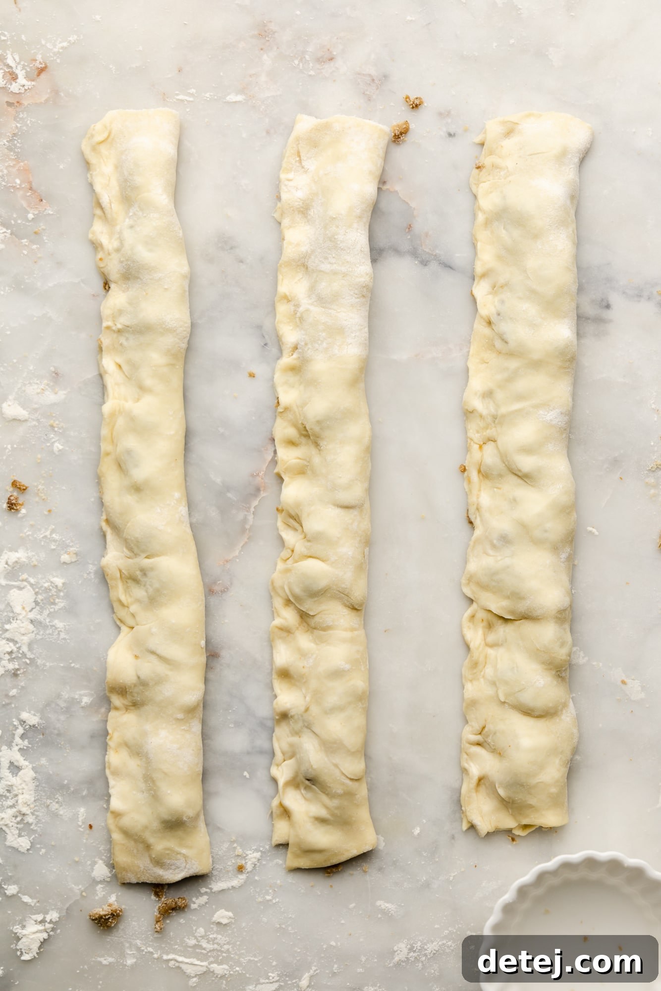 Close-up of neatly folded strips of puff pastry, filled with vegan sausage crumbles, before baking.