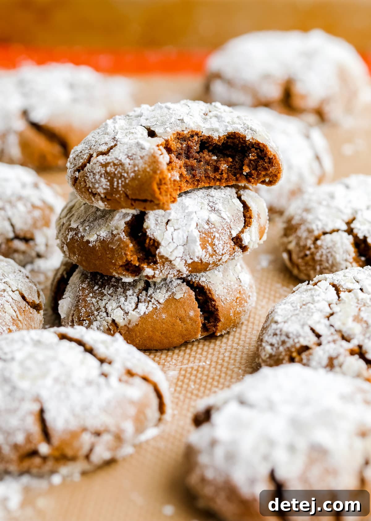 Stack of three ginger crinkle cookies with powdered sugar, resting on a silicone baking mat.