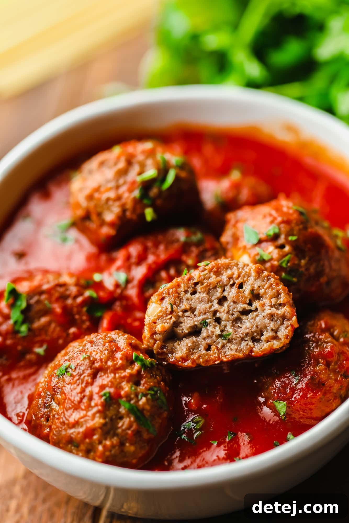 Next-Gen Meatballs 9 A vegan meatball, perfectly cut in half, rests atop a generous pile of marinara sauce-covered vegan meatballs, showcasing its meaty interior.