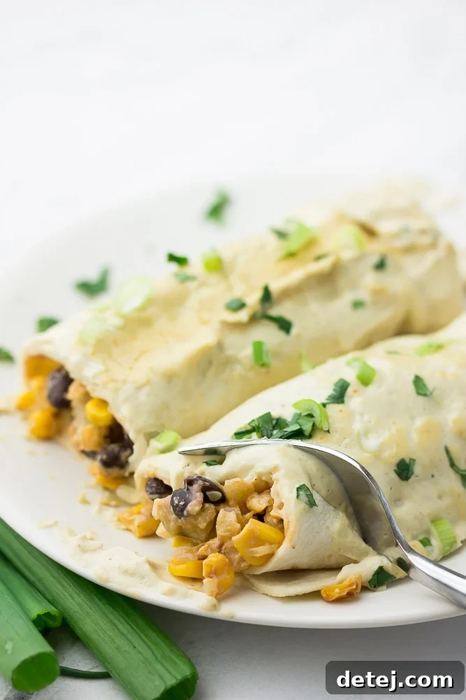 A fork cutting into a white enchilada on a plate, revealing the flavorful vegetable and bean filling inside.