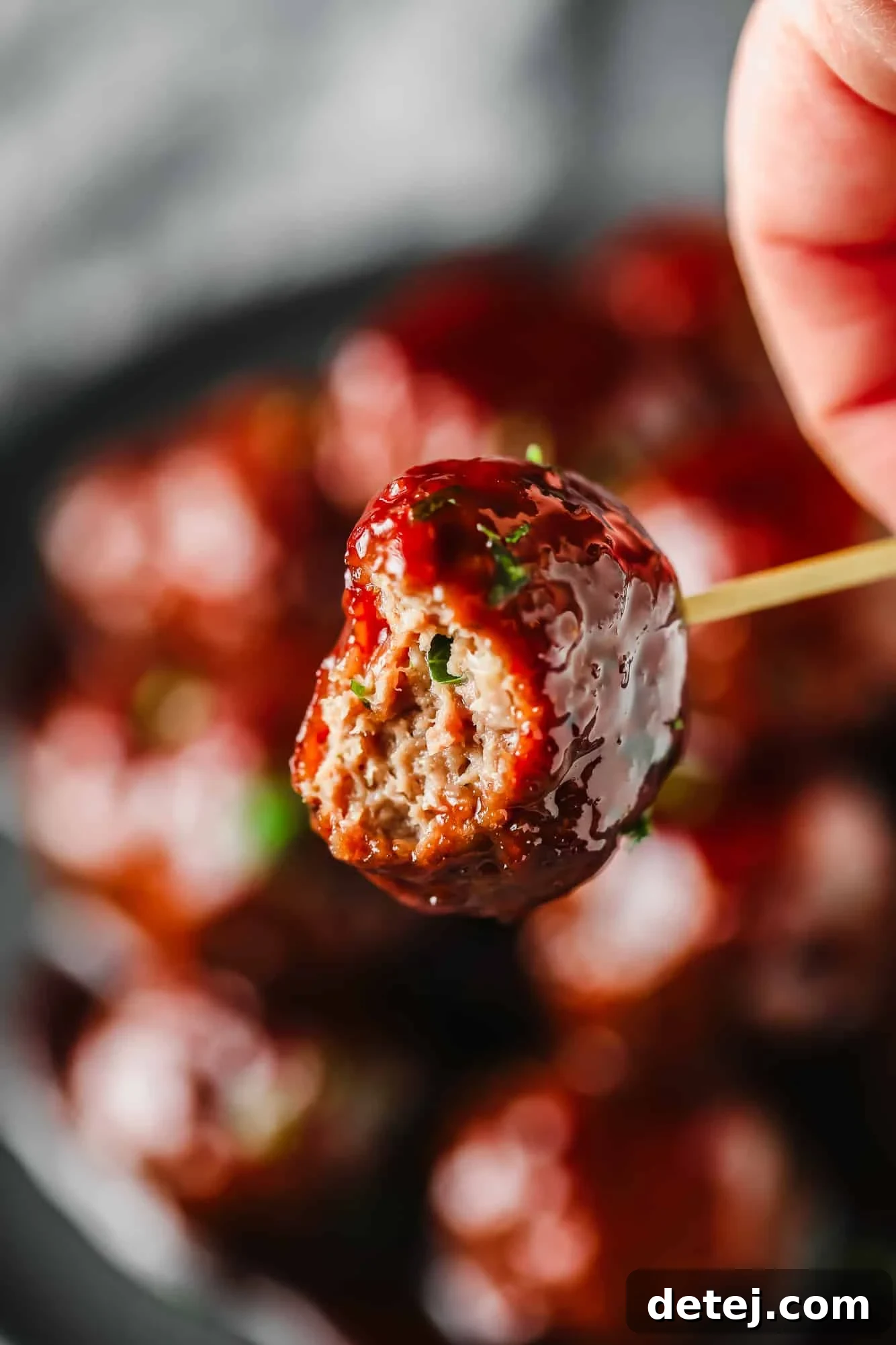A close-up shot of a single vegan grape jelly meatball, with a small bite taken out, revealing its juicy interior and sticky glaze.