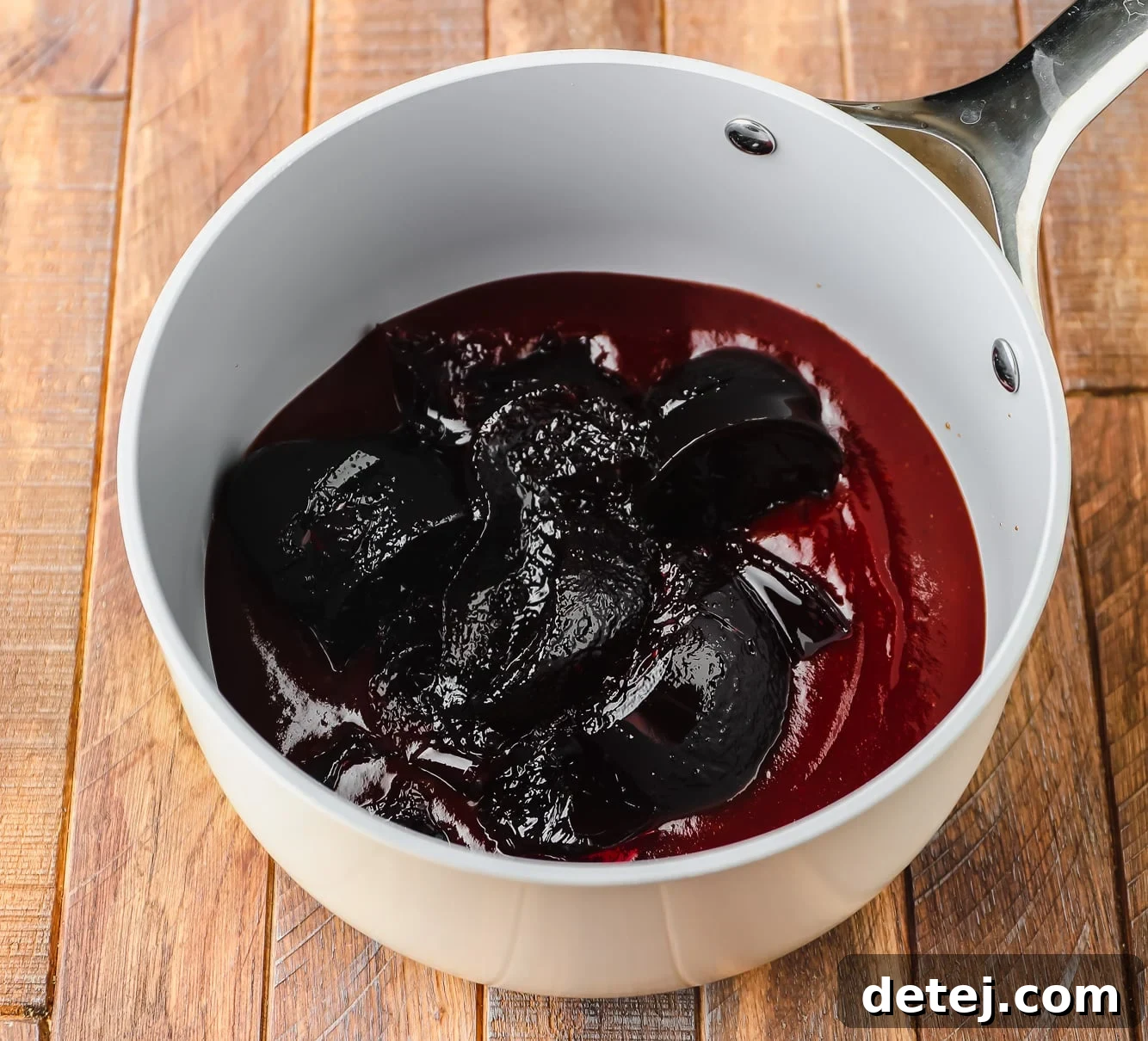A grey saucepan with rich, dark BBQ sauce and shimmering purple grape jelly poured in, ready to be mixed and heated.