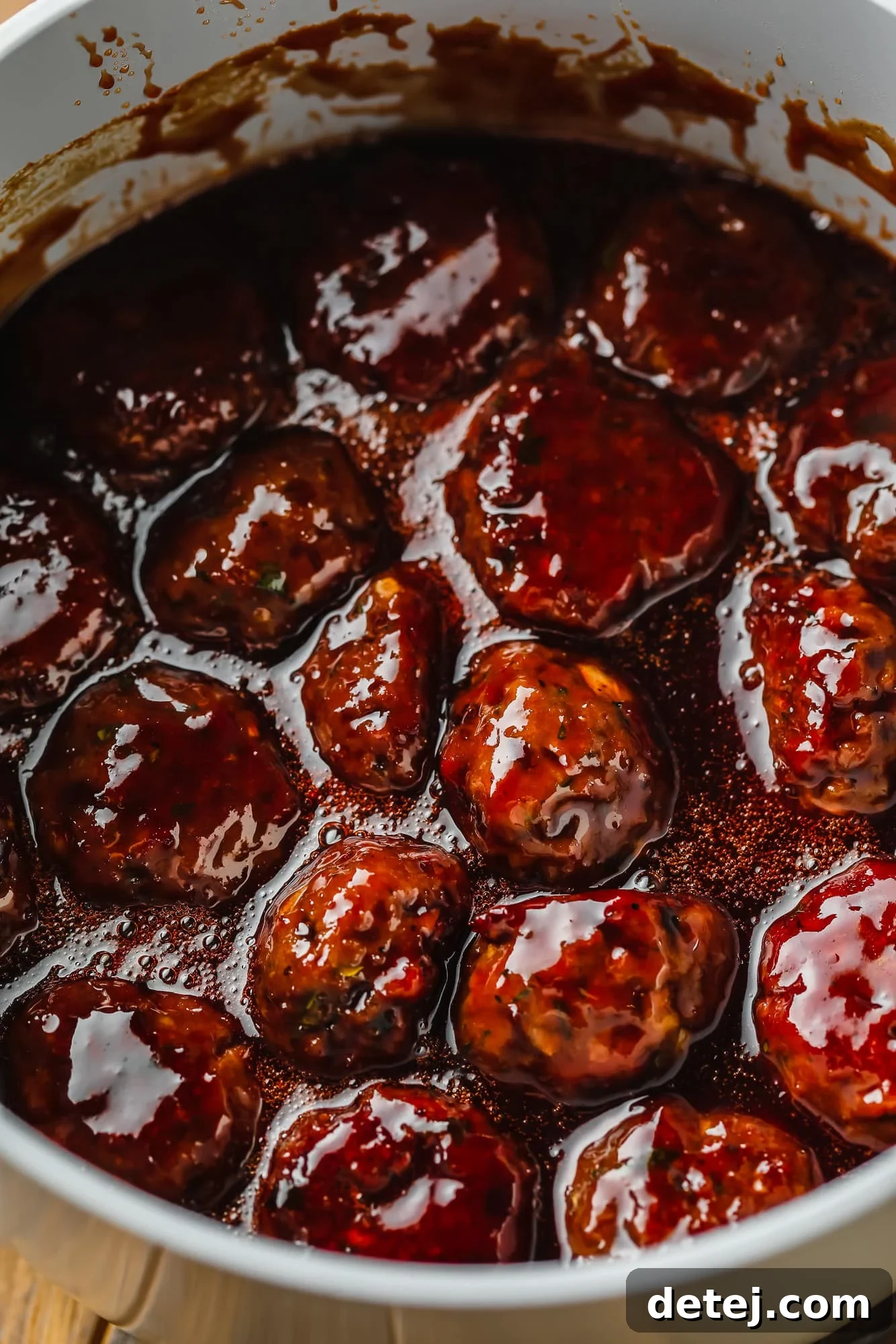 A saucepan filled with vegan meatballs generously coated in a rich, dark grape jelly and BBQ sauce, simmering gently on the stove.