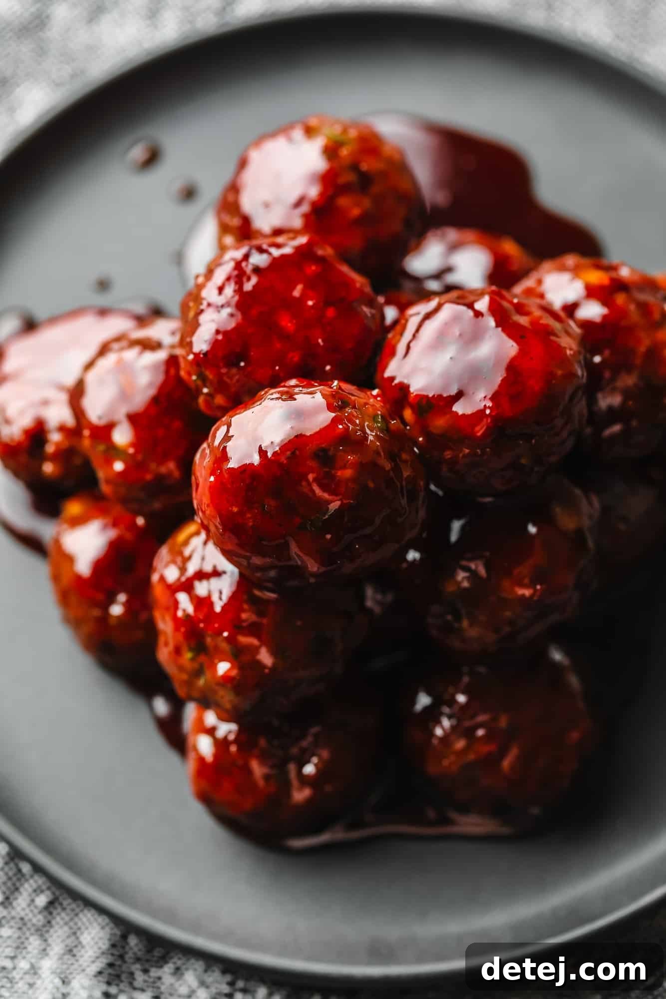 A generous pile of vegan grape jelly meatballs resting on a simple grey plate, showcasing their glossy, appetizing coating.