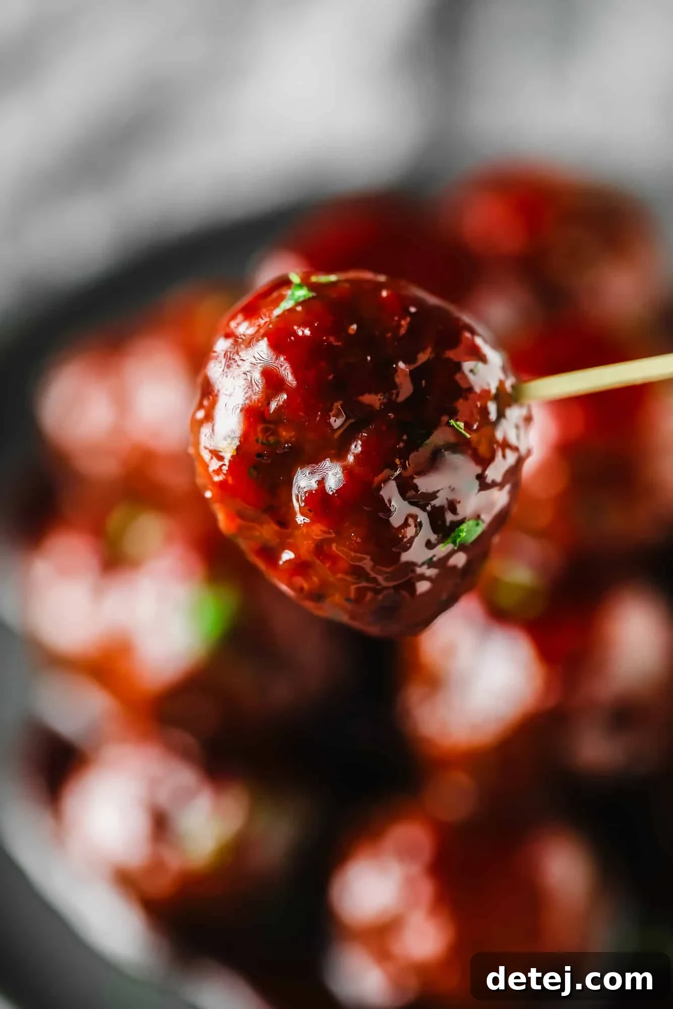 A close-up of a single vegan grape jelly meatball, glistening with sauce, resting on a grey surface.