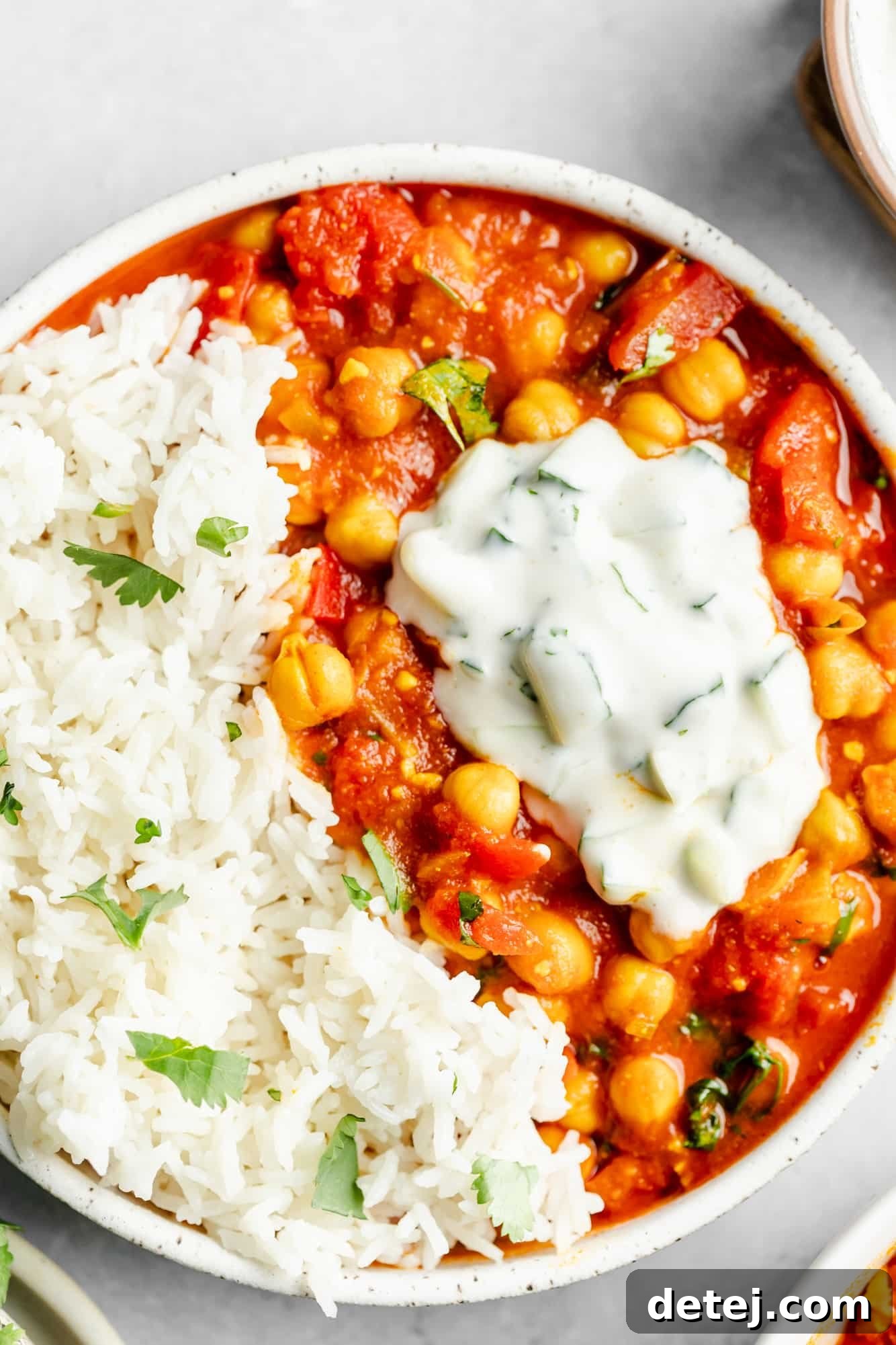 vegan chana masala in a bowl with rice and topped with a dollop of raita.