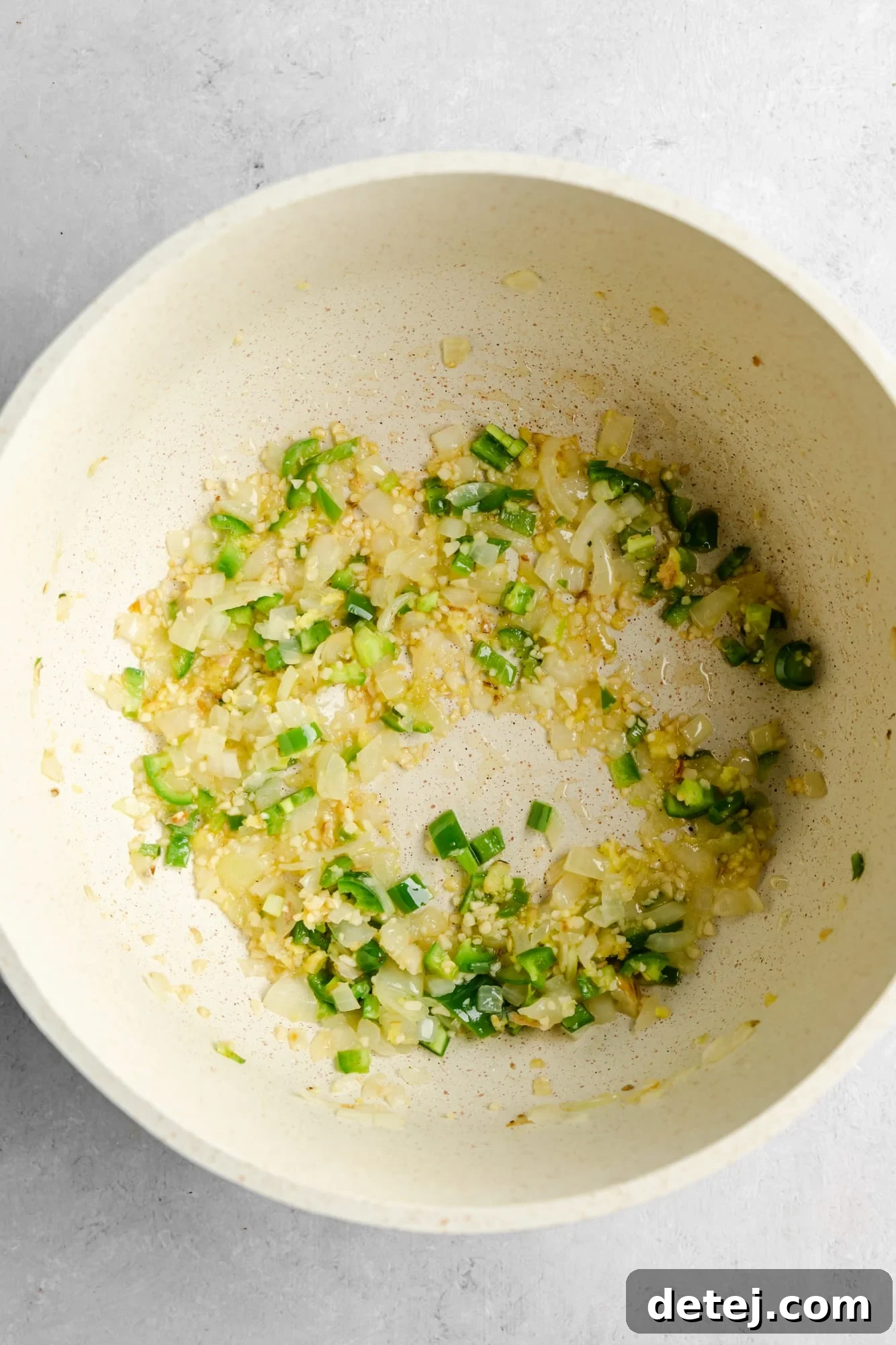 sauteeing onion, garlic, ginger, and green peppers in a large white pot.