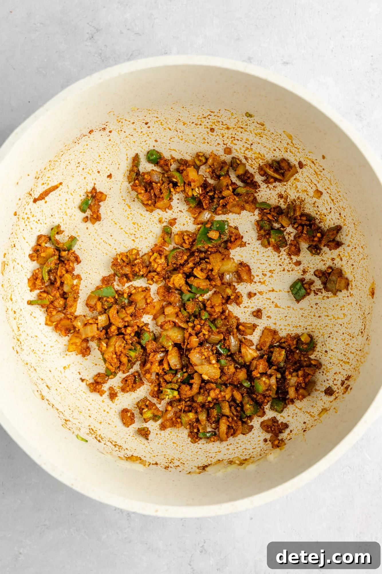cooked aromatics covered in spices in a large white pot.