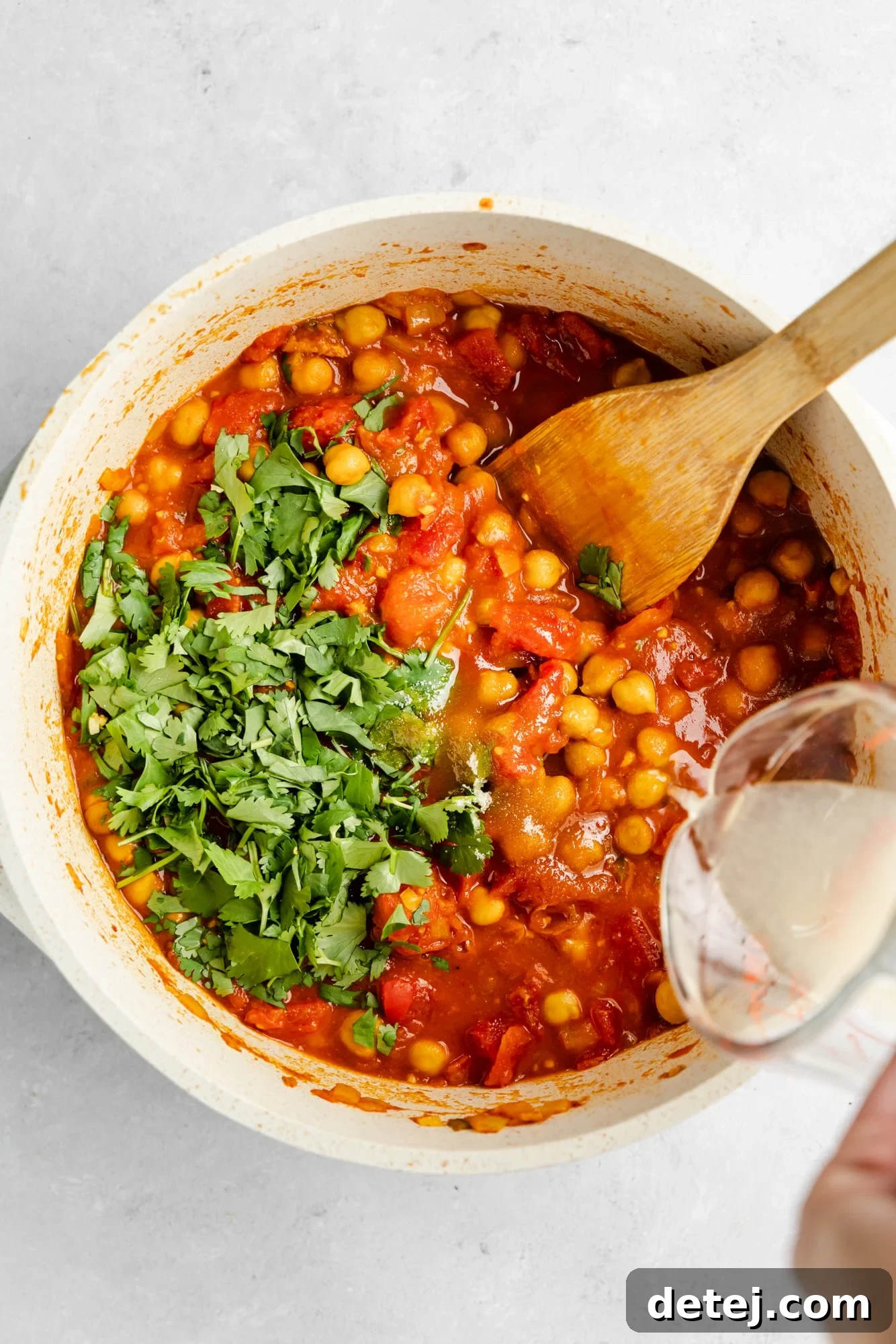 pouring lemon juice into a large pot filled with chana masala.