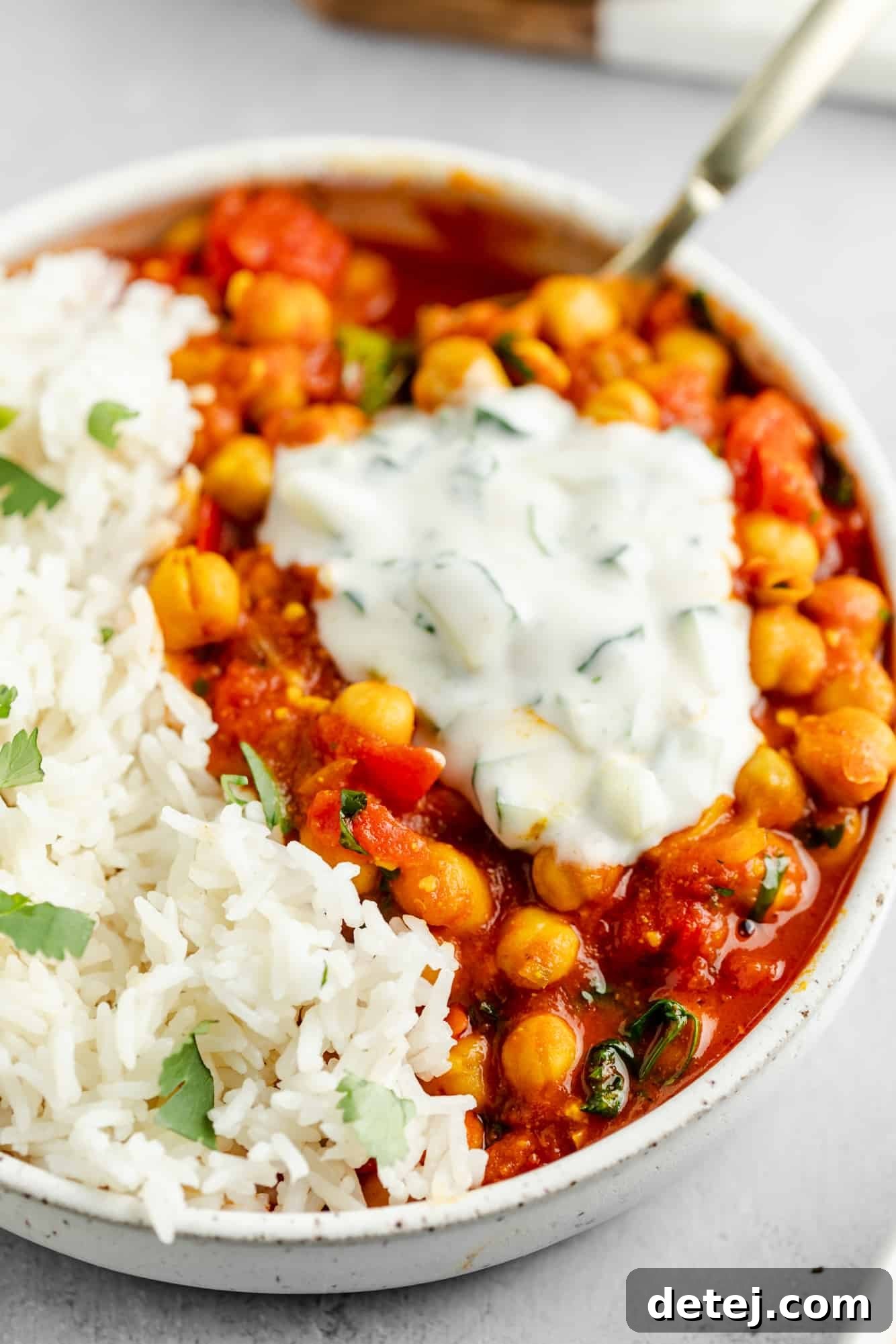 vegan chana masala in a bowl with rice and topped with a dollop of raita.