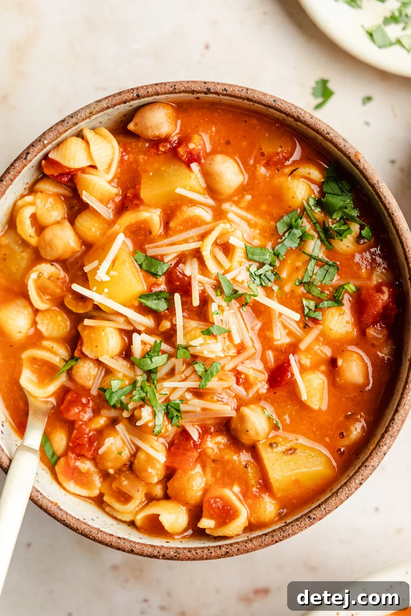 Italian chickpea soup topped with vegan parmesan and parsley in a bowl, showcasing its rich texture and vibrant garnish.