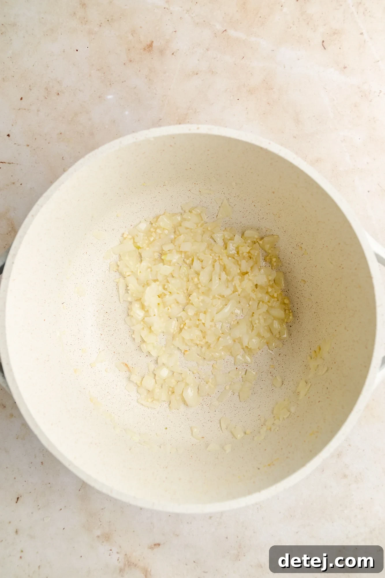 Sautéing diced onion and minced garlic in olive oil in a large white soup pot, emitting a fragrant steam.