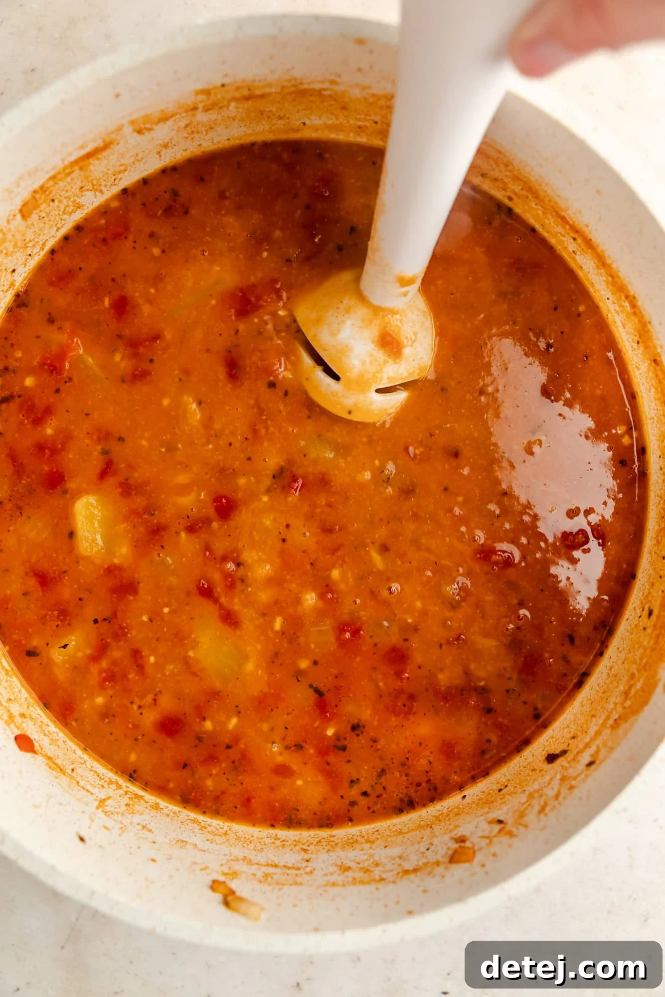 An immersion blender being used to blend chickpea soup directly in a large white pot, creating a smooth and creamy texture.