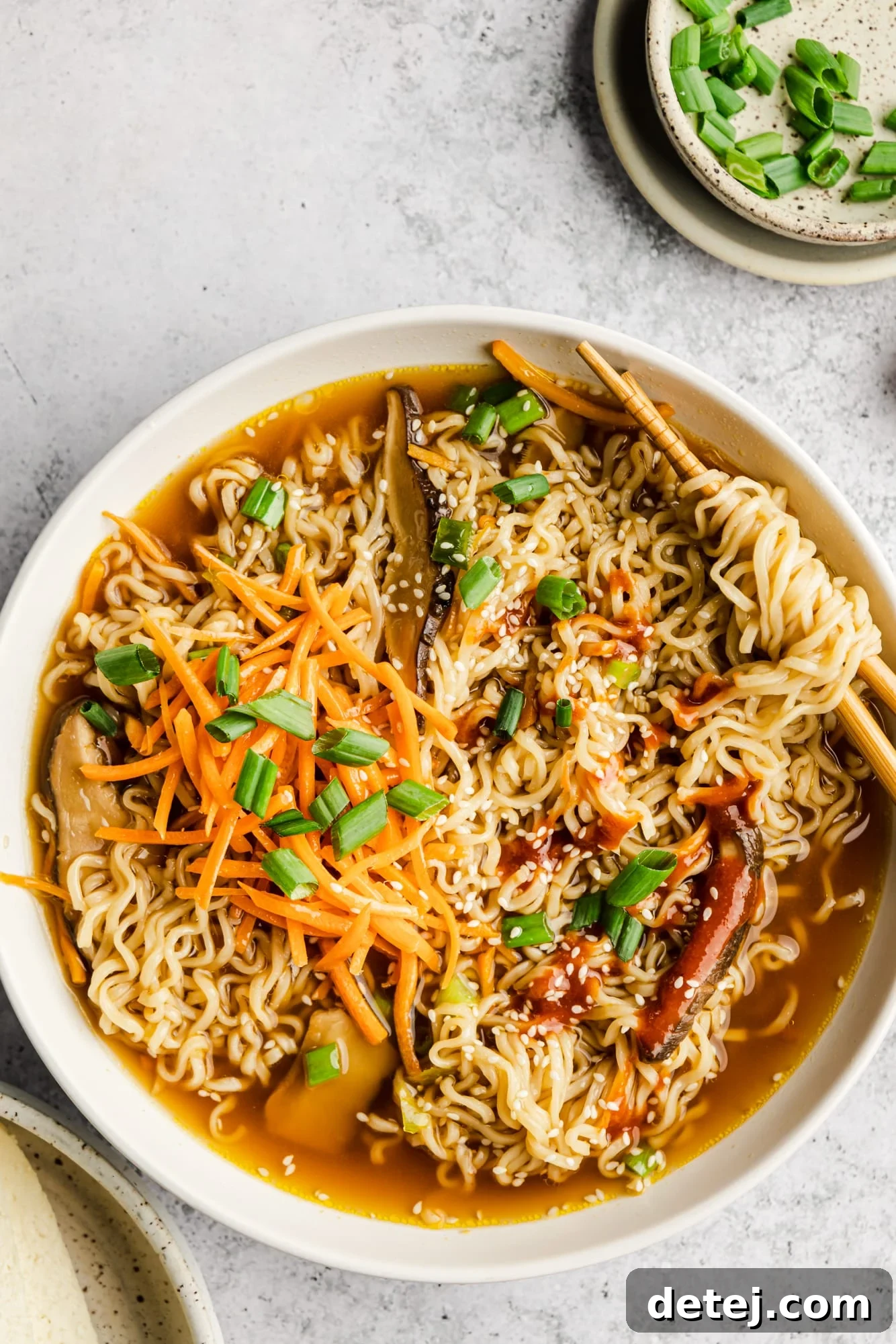 A large white bowl brimming with steaming vegan ramen, complete with chopsticks resting on the rim.
