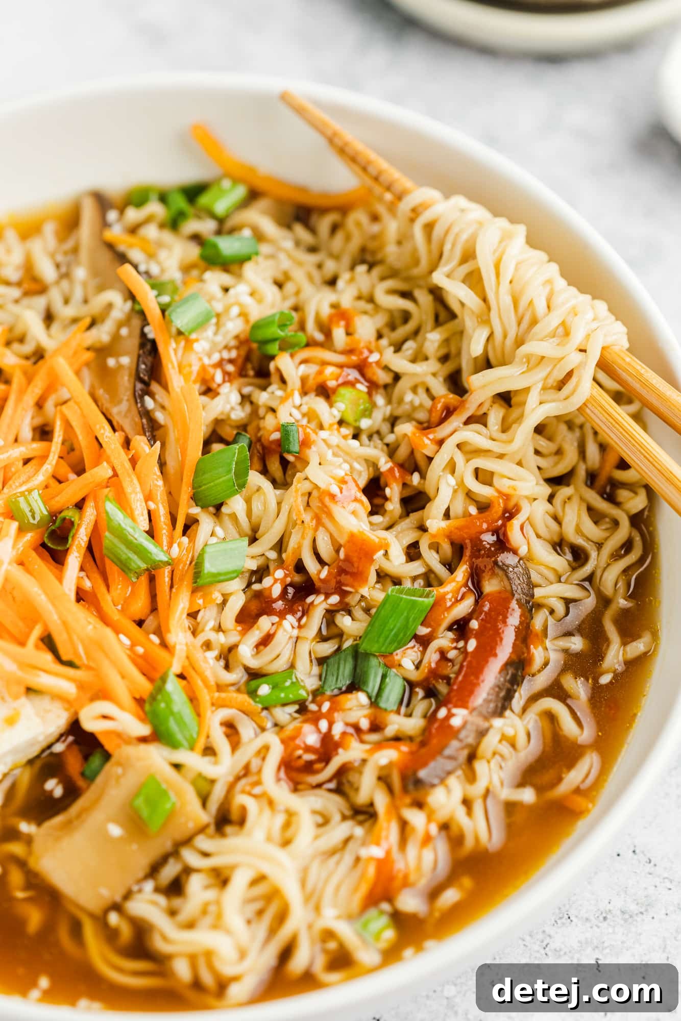 Another perspective of the vegan ramen in a large white bowl, garnished with fresh scallions and chili flakes, ready to be enjoyed with chopsticks.