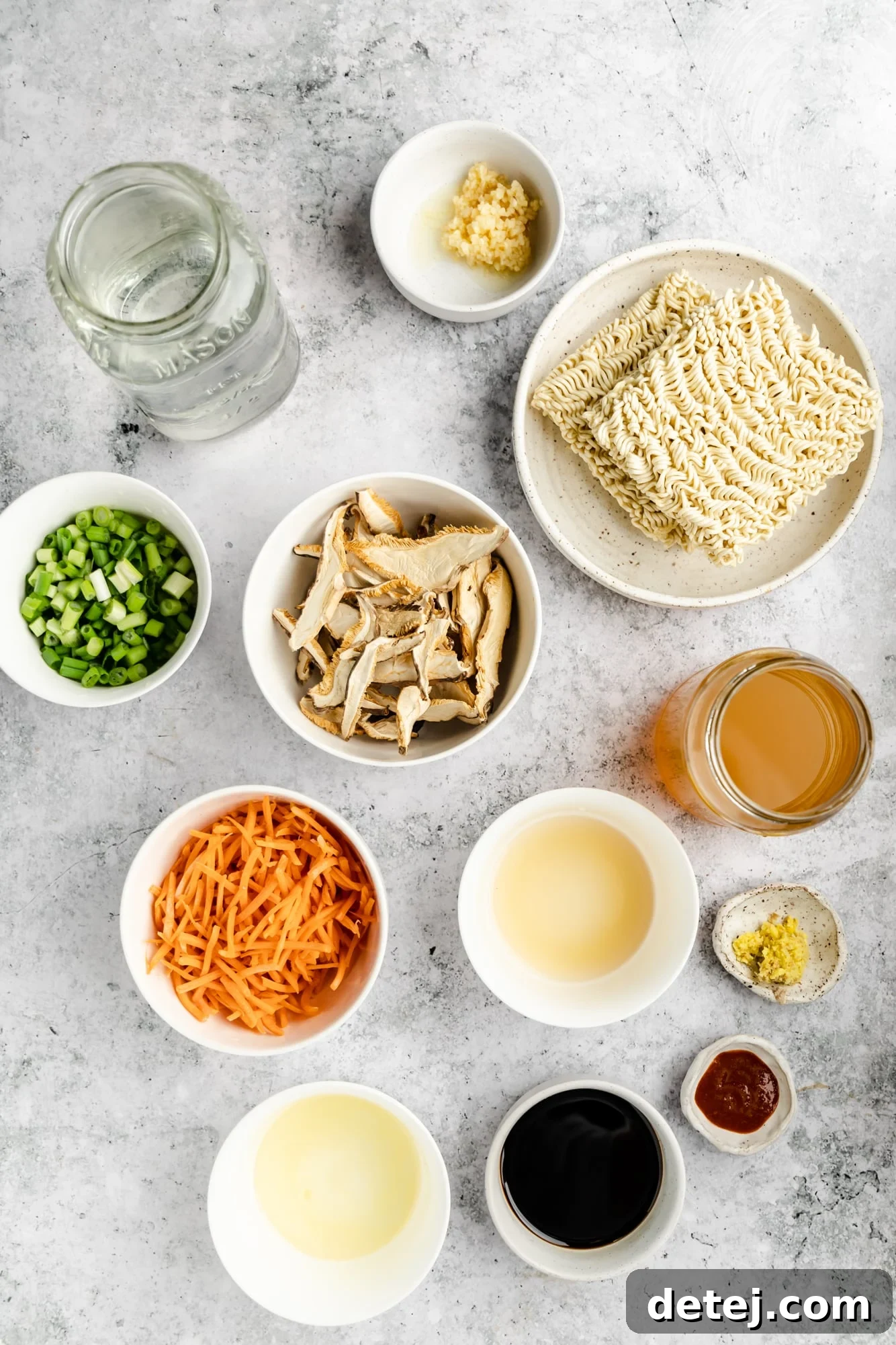 Individual white bowls showcasing the fresh ingredients laid out for making easy vegan ramen, including sliced mushrooms, shredded carrots, ginger, garlic, and scallions.