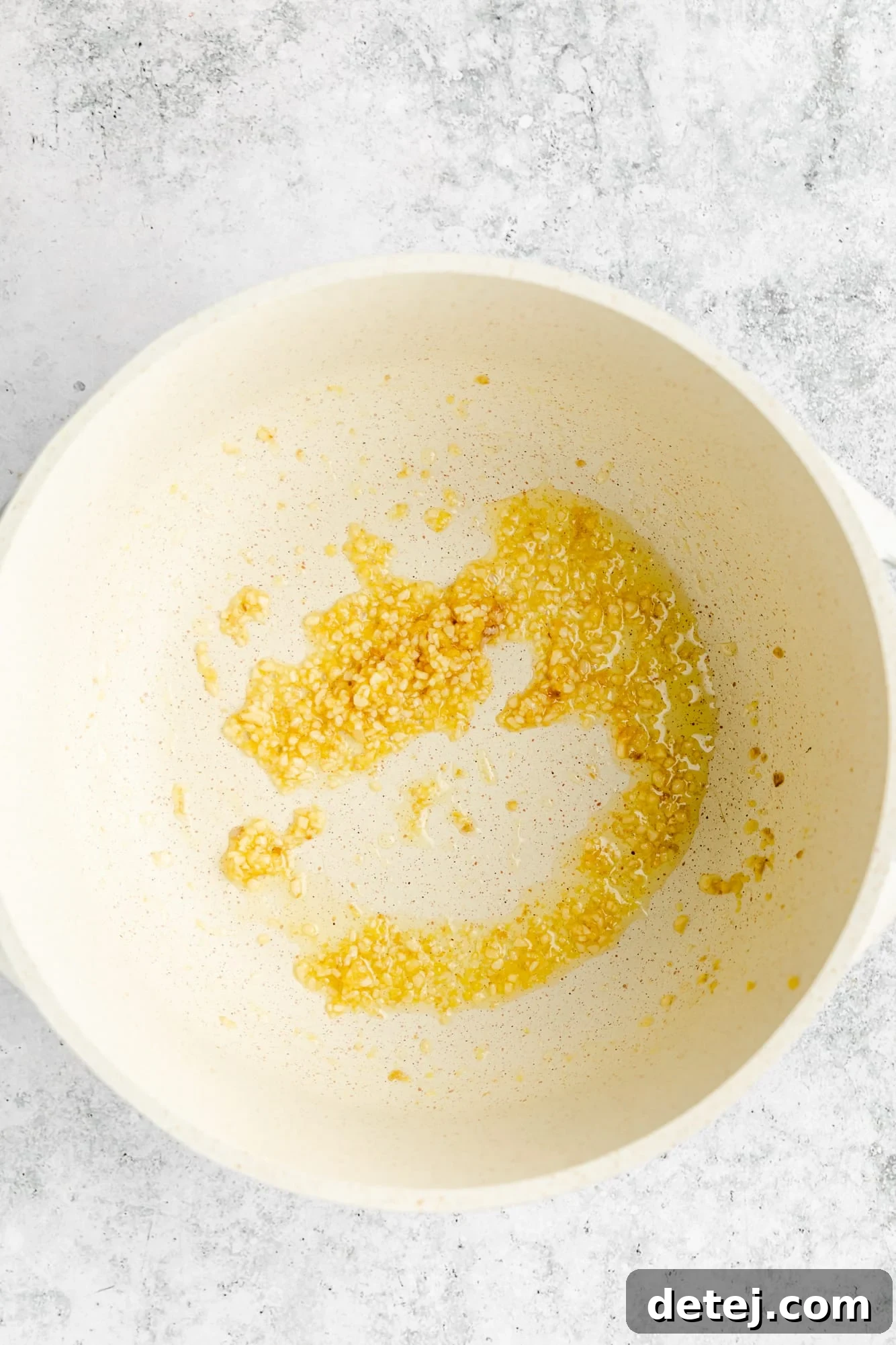 Close-up shot of garlic and ginger being sautéed in sesame oil in a white pot, emitting a fragrant steam.