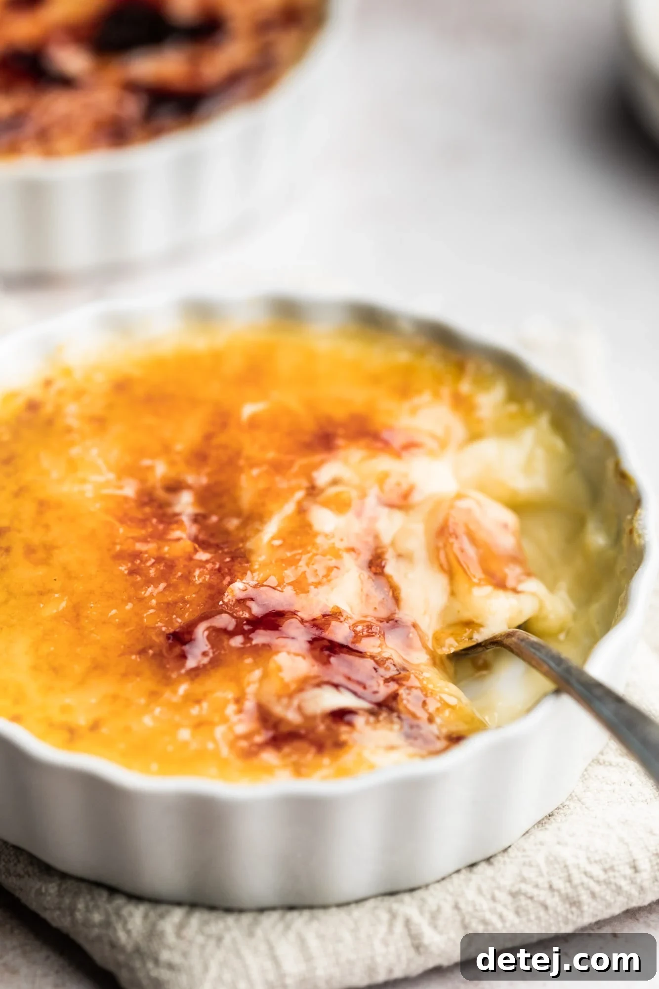 A metal spoon scooping a bite of golden-brown Vegan Creme Brulee from a white ramekin.