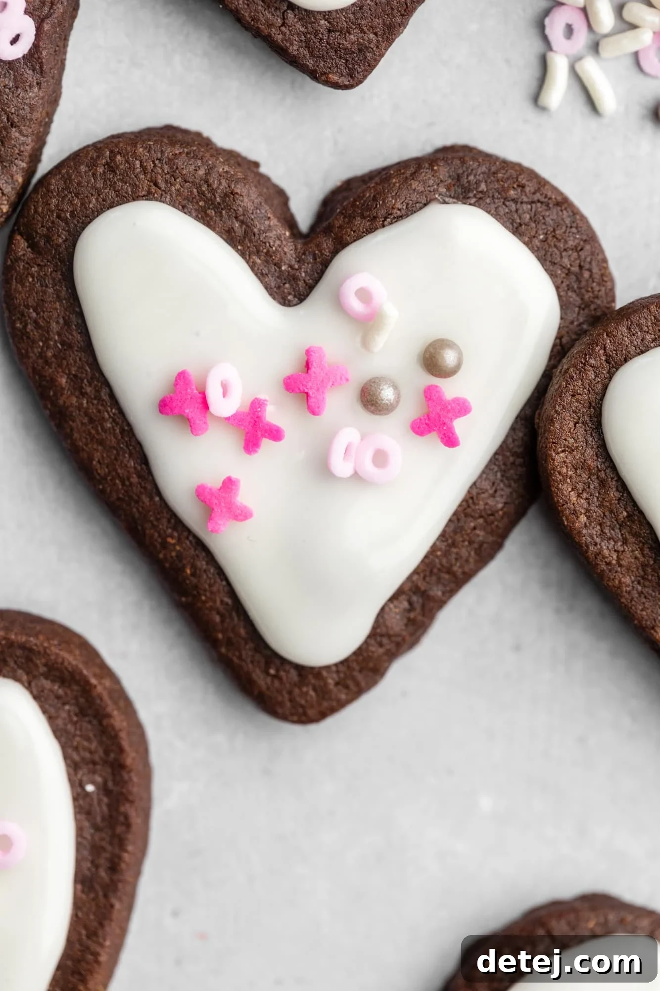 heart-shaped chocolate sugar cookies decorated with white icing and pink sprinkles.