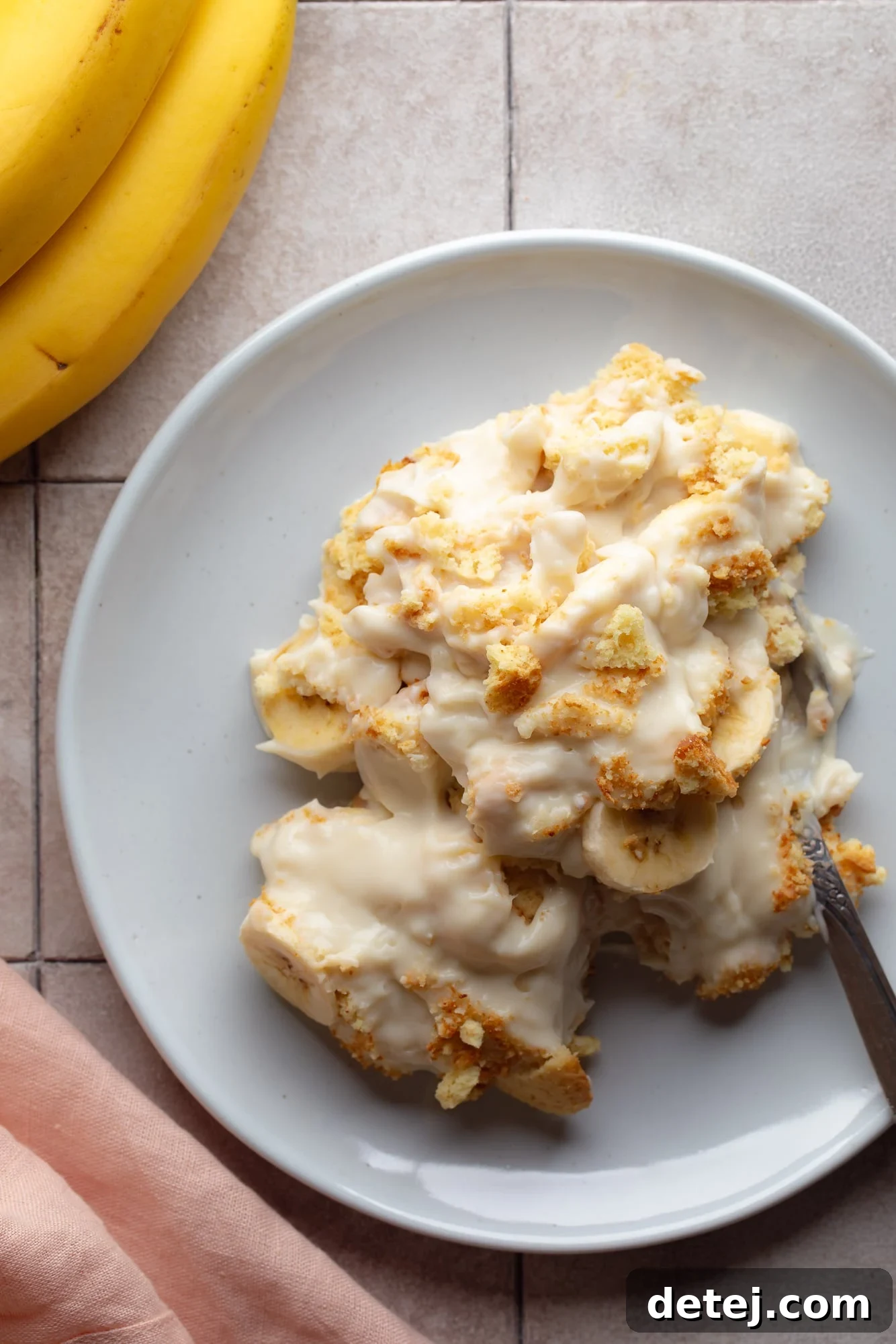 A beautifully plated vegan banana pudding, showcasing creamy custard, fresh banana slices, and crumbled vanilla wafer cookies on a sophisticated grey background.