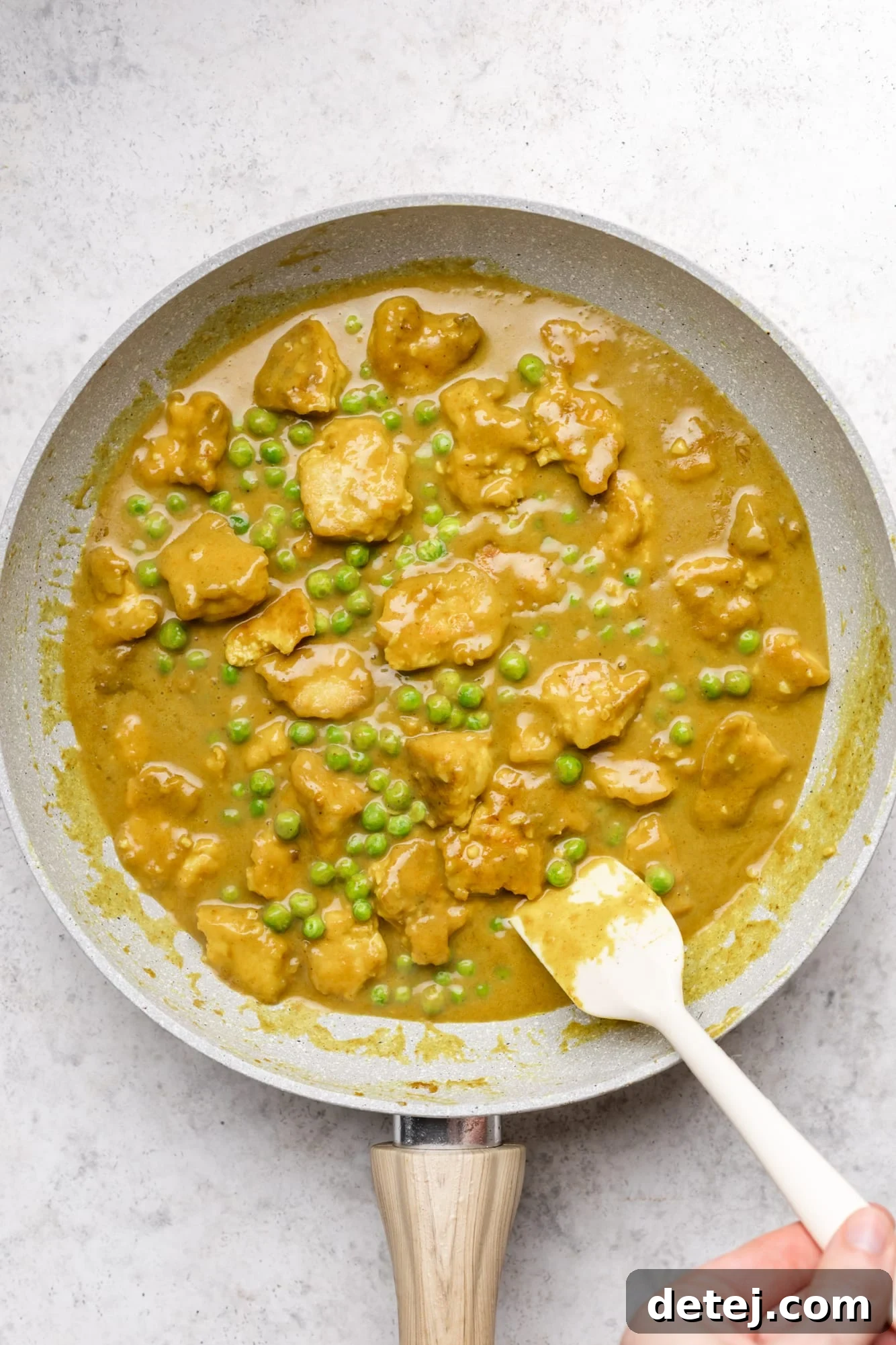 stirring yellow tofu curry in a grey pan with a white spatula.