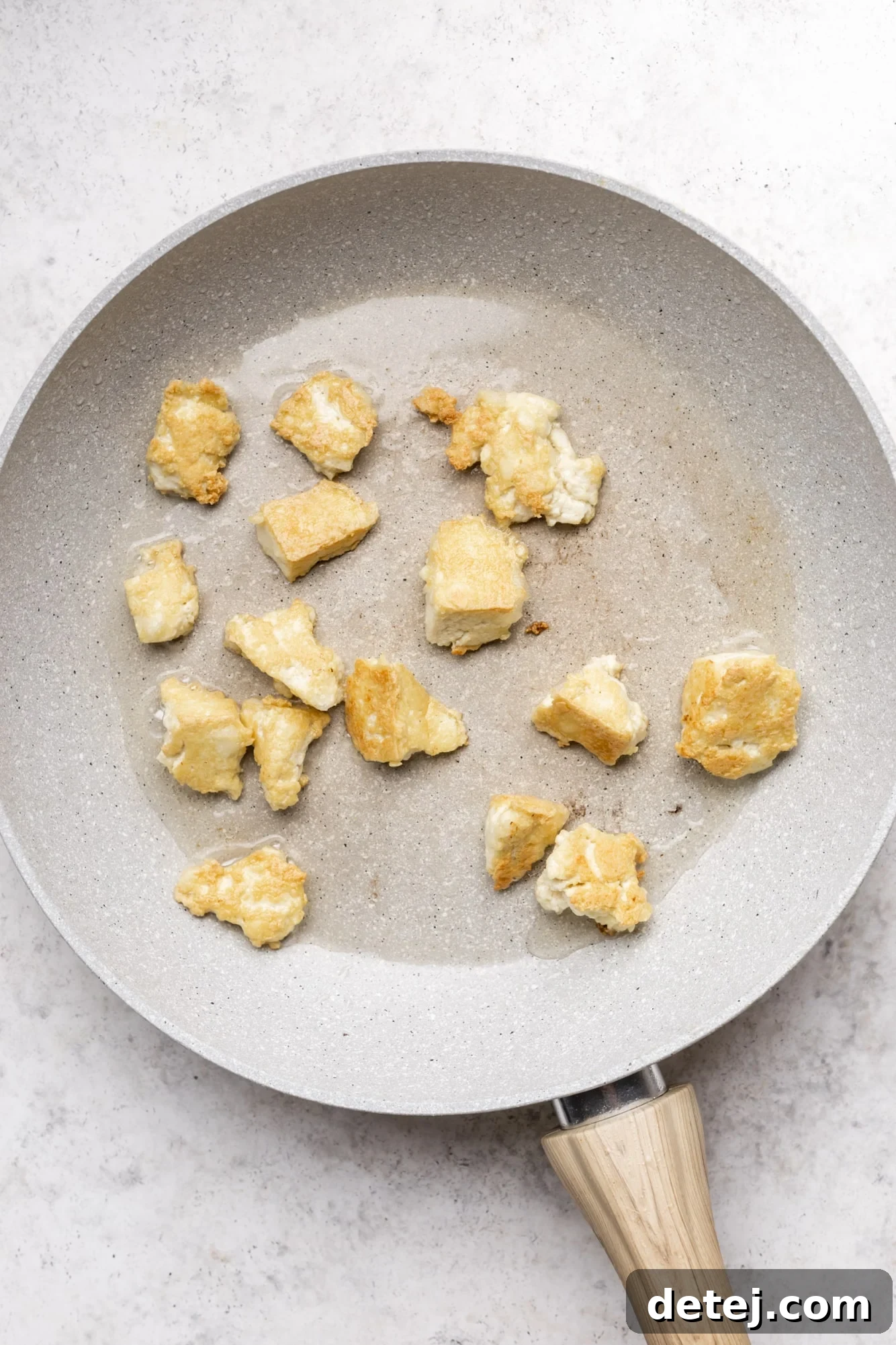frying tofu chunks in an oiled grey pan.