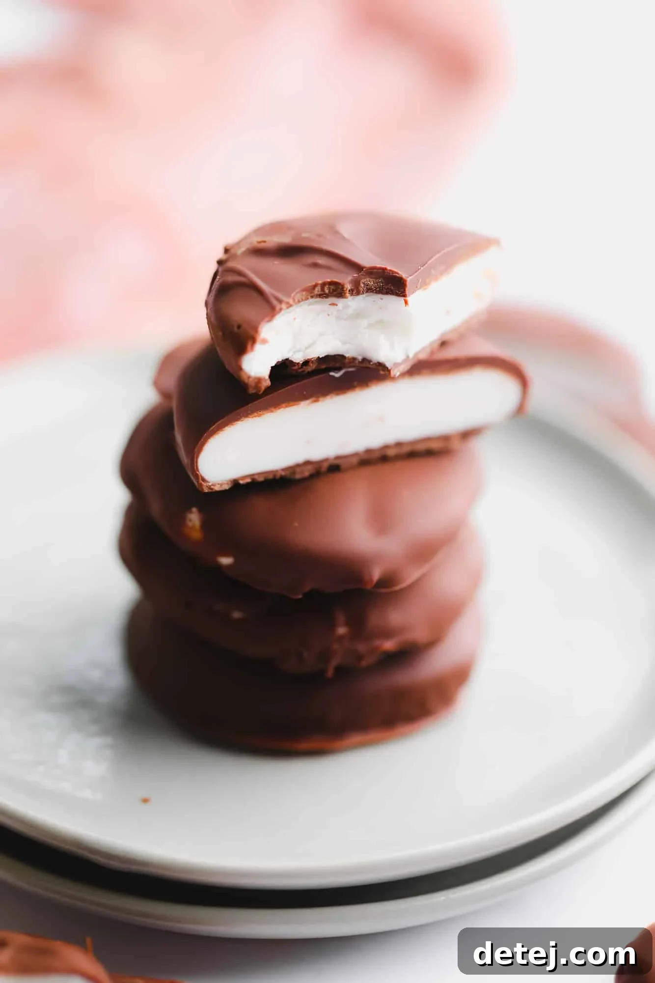 A beautifully arranged stack of vegan peppermint patties, some cut in half to reveal their creamy minty center, resting on a small plate.