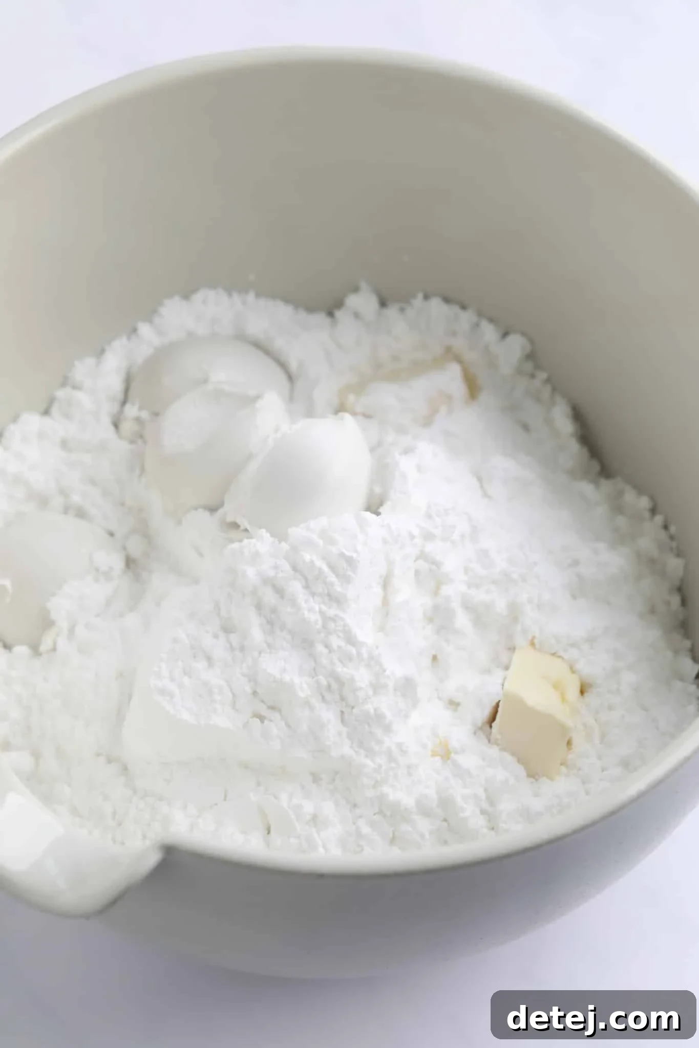 Powdered sugar, solid coconut milk cream, and vegan butter, ready to be combined in a large white mixing bowl.