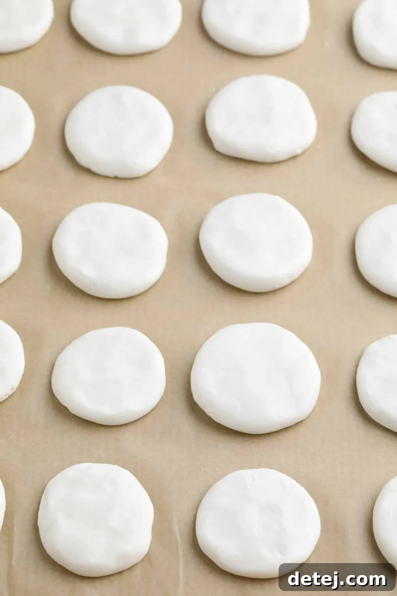 Rows of firm, white peppermint discs neatly arranged on a parchment-lined baking sheet, ready for their chocolate coating.
