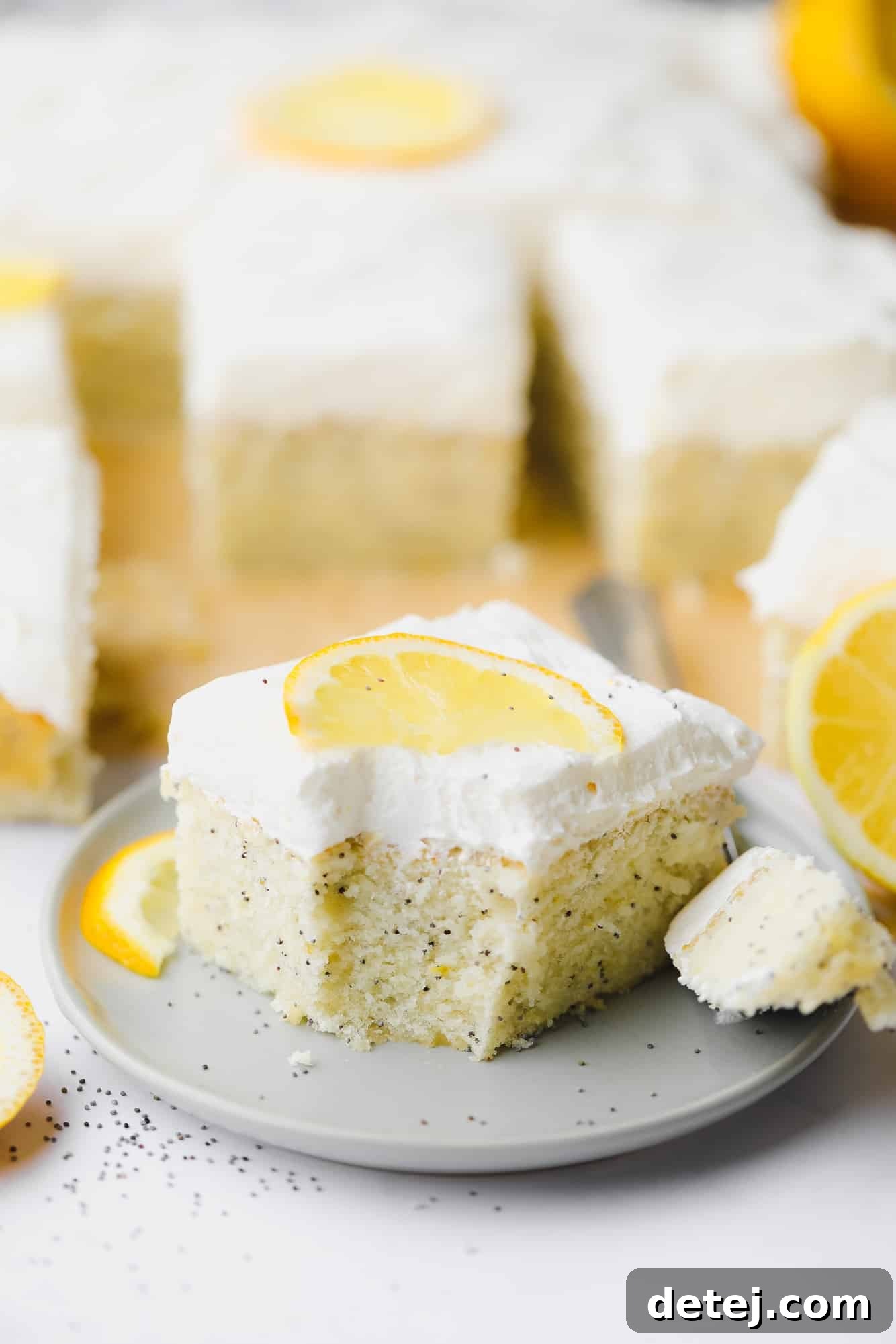 A perfectly sliced piece of vegan lemon poppyseed cake, adorned with whipped lemon buttercream, sits on a small grey plate with a bite removed, showcasing its moist, fluffy crumb.