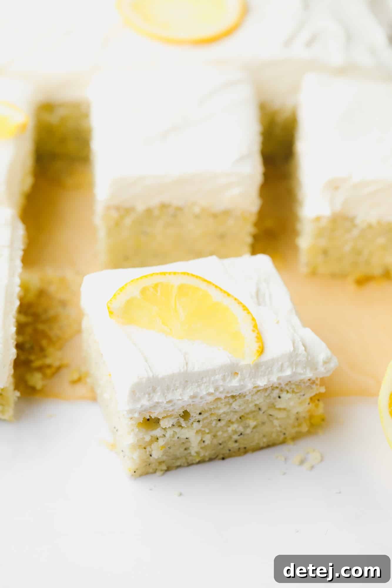 A generous slice of fluffy vegan lemon poppyseed cake, topped with a swirl of lemon buttercream and a thin slice of fresh lemon, ready to be enjoyed.