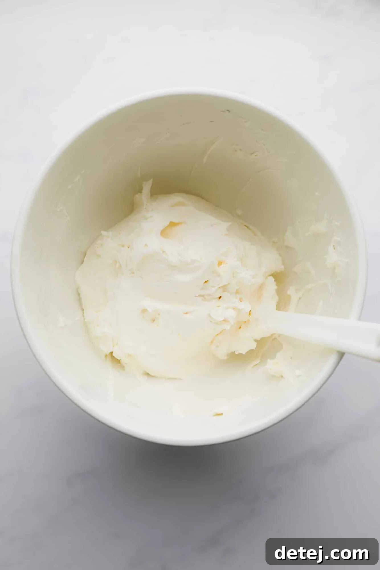 Smooth, creamy white buttercream frosting, perfectly whipped and ready to be spread, fills a large white mixing bowl.