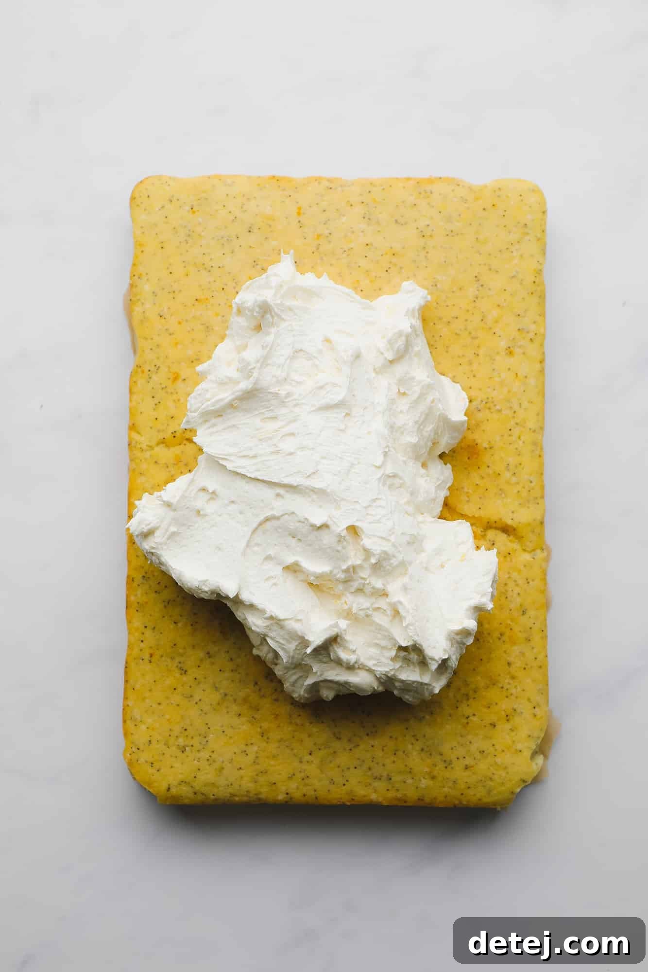 A generous, swirling mound of white buttercream frosting expertly applied to the top of a freshly baked, rectangular lemon poppyseed cake.