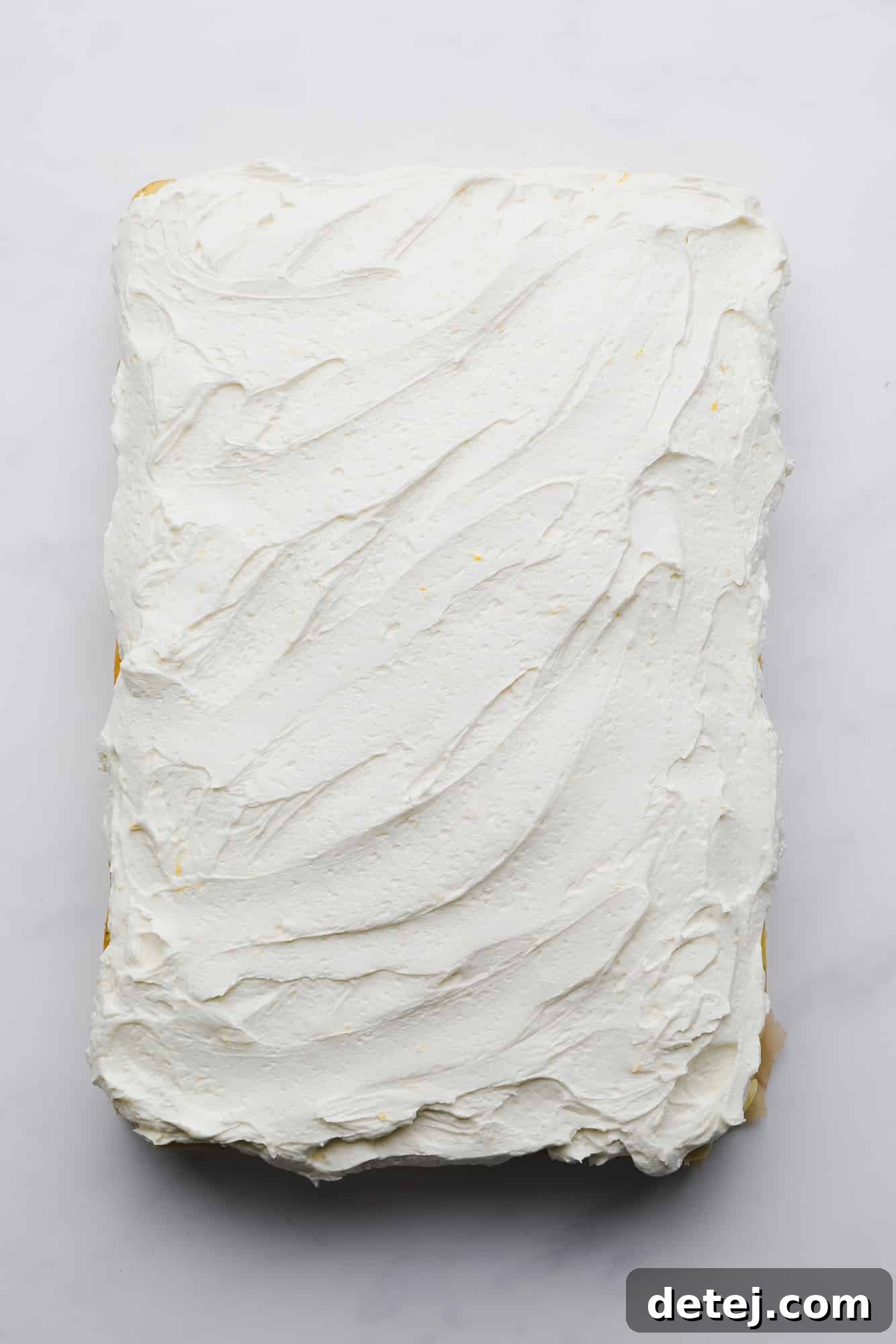 A delightful lemon poppyseed cake, generously covered with smooth, white lemon icing, presented whole and ready to be sliced.