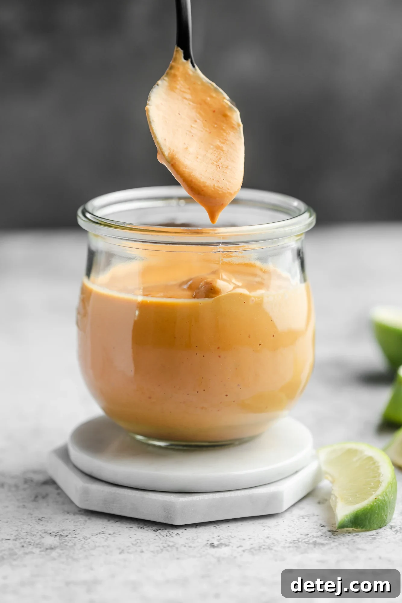Smoky Chipotle Magic 2 A spoon lifting up a vibrant orange chipotle sauce from a small glass jar, highlighting its creamy texture.