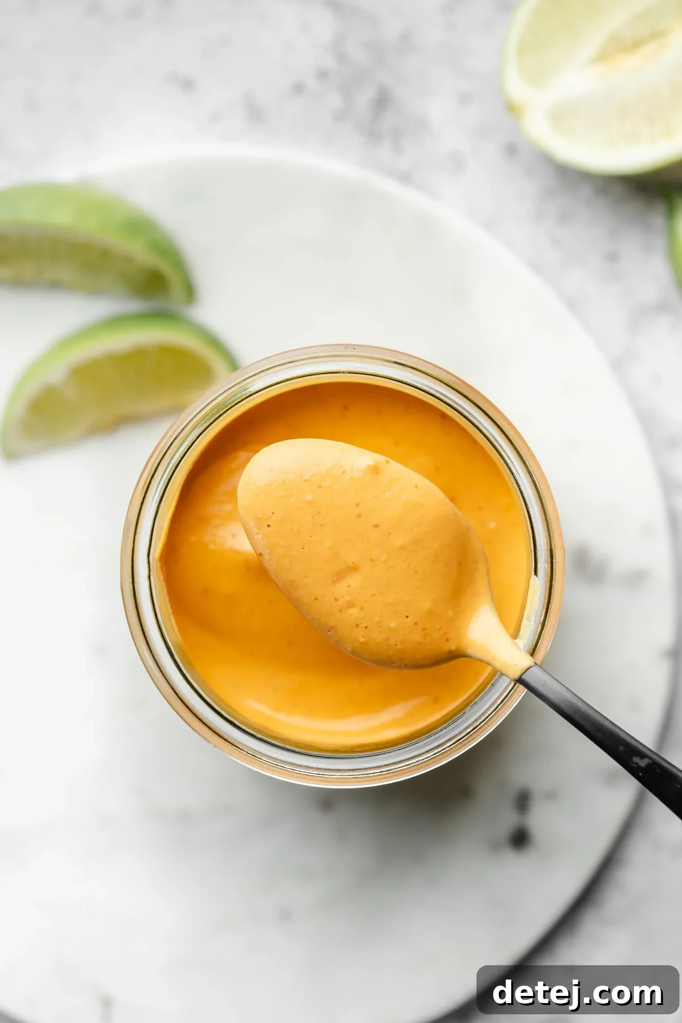 Smoky Chipotle Magic 7 A spoon lifting a perfect scoop of orange chipotle sauce from a glass jar, showing its thickness.