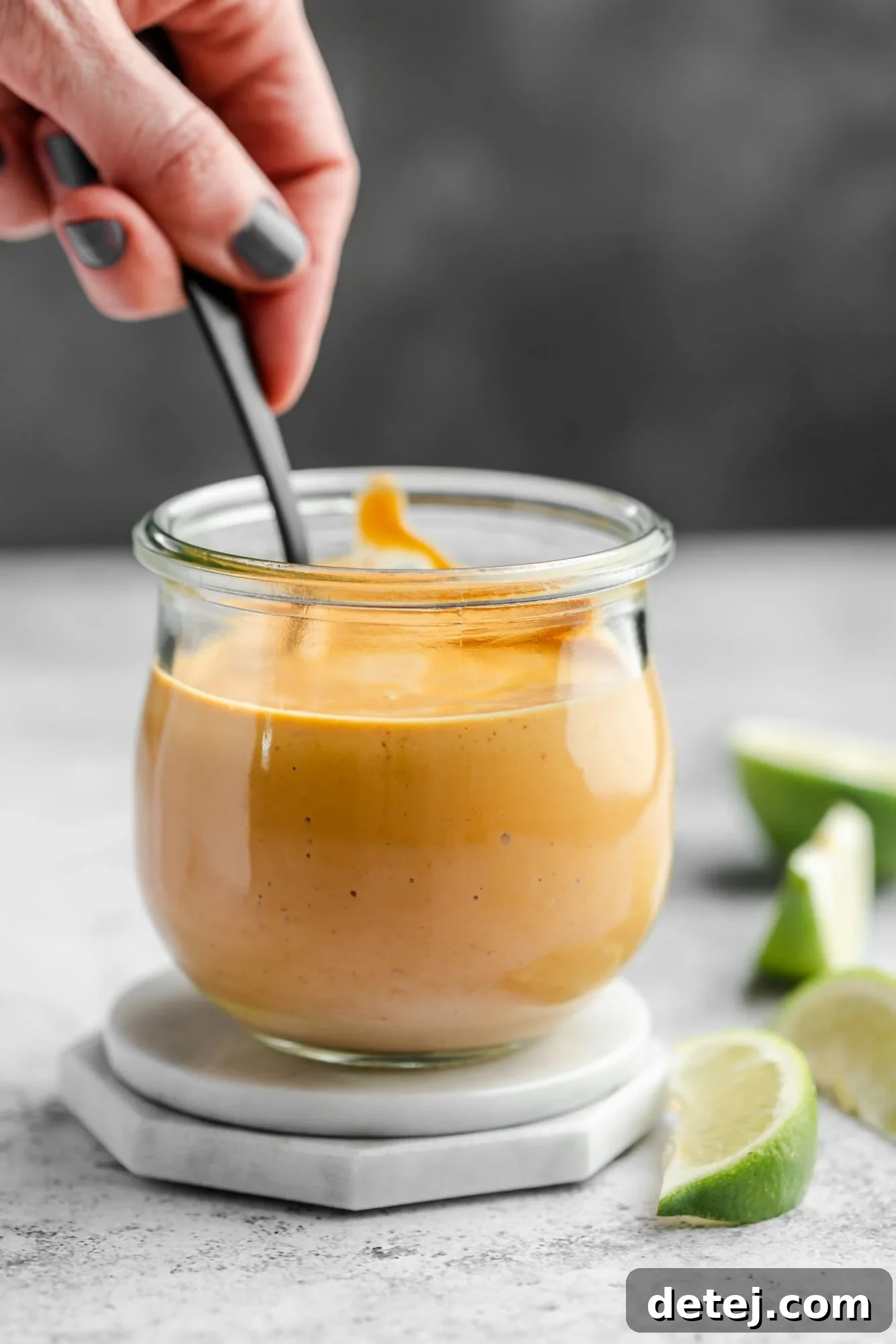 Smoky Chipotle Magic 8 A woman's hand gently holding a spoon in a jar of rich orange chipotle sauce.