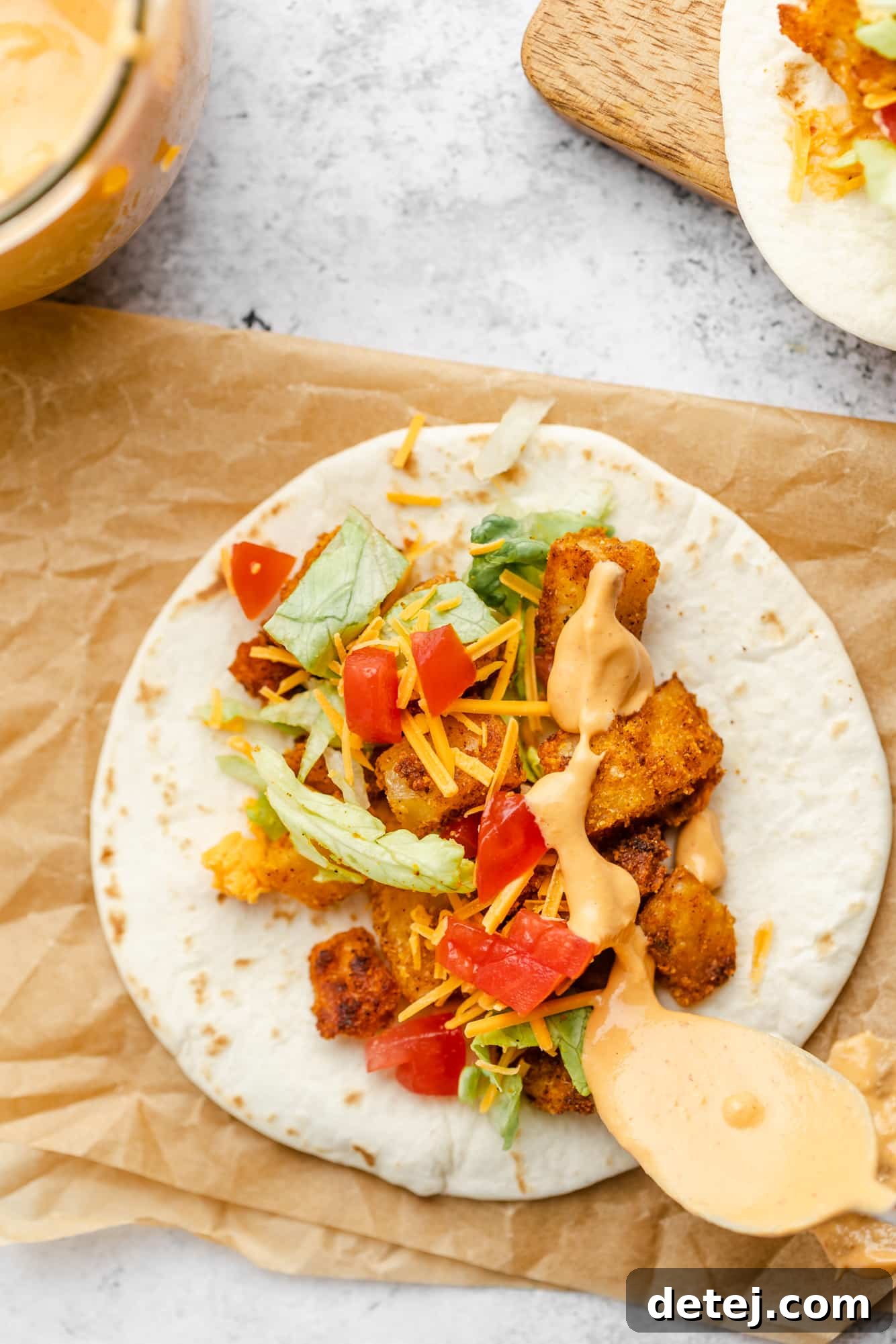 A close-up shot of a hand drizzling creamy vegan chipotle sauce over a beautifully assembled spicy potato taco.