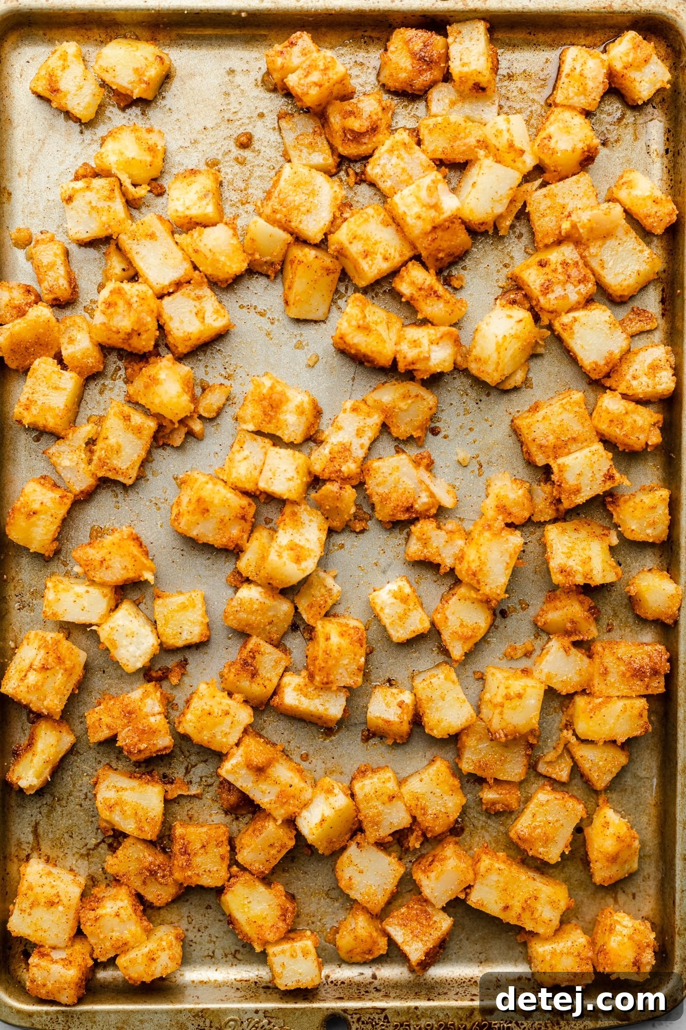 Evenly spaced, seasoned potato chunks laid out on a large baking sheet, ready for the oven.
