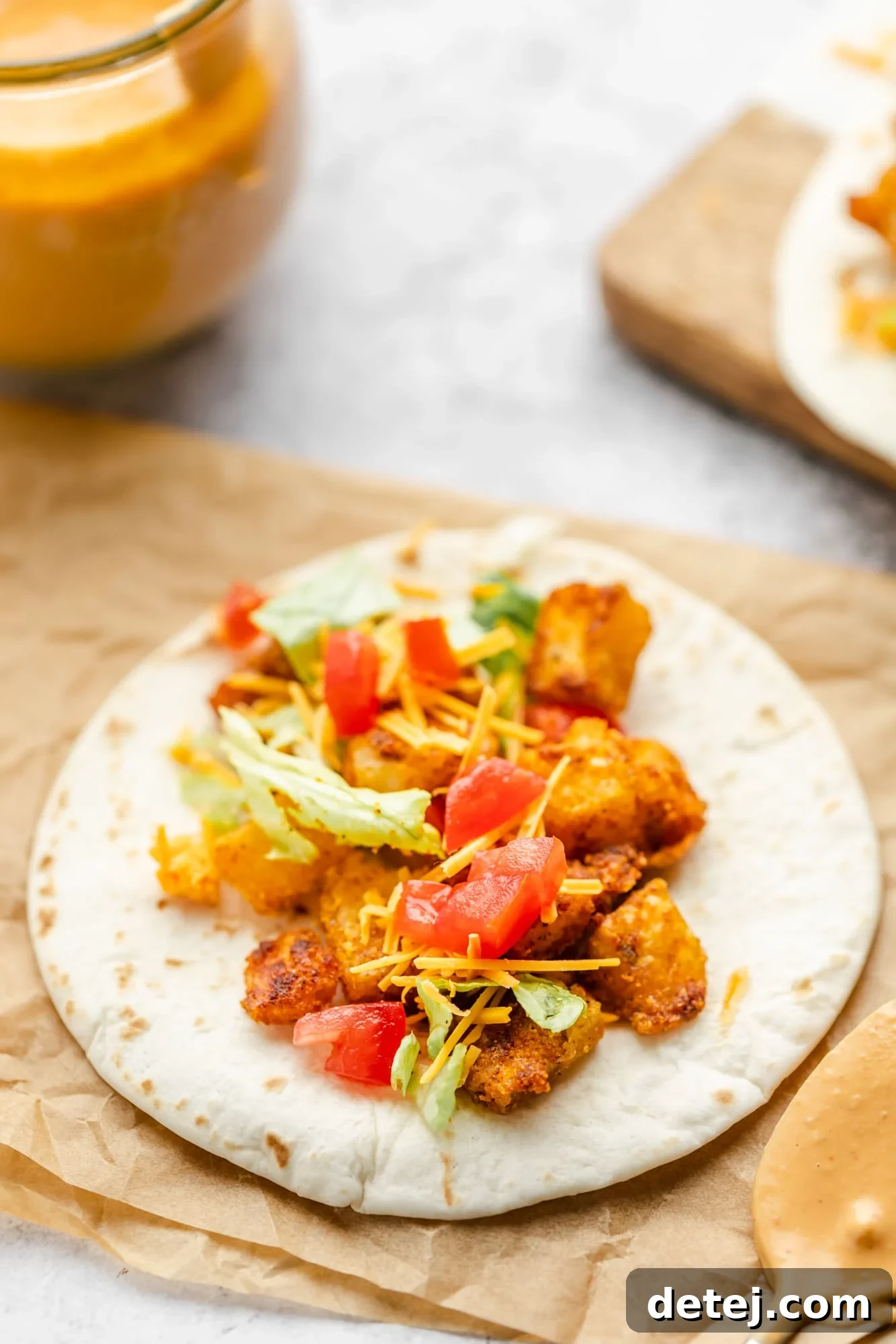 A small flour tortilla artfully arranged with crispy potatoes, diced tomatoes, shredded lettuce, and vegan cheese.